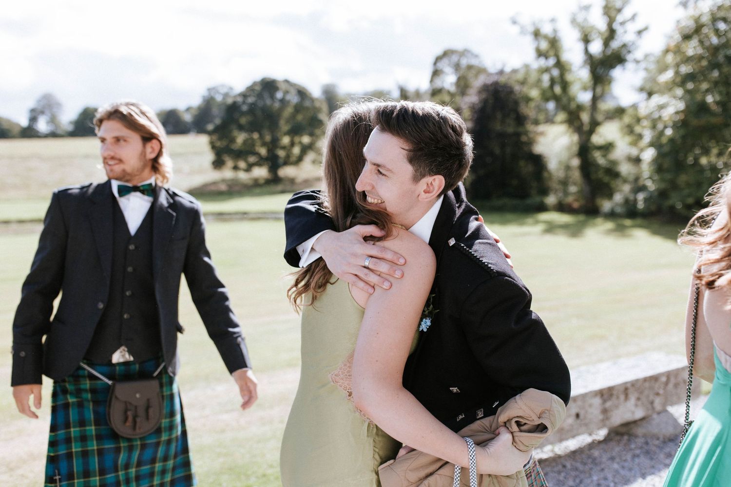 Wedding party members embracing and celebrating on castle grounds during a sunny day.