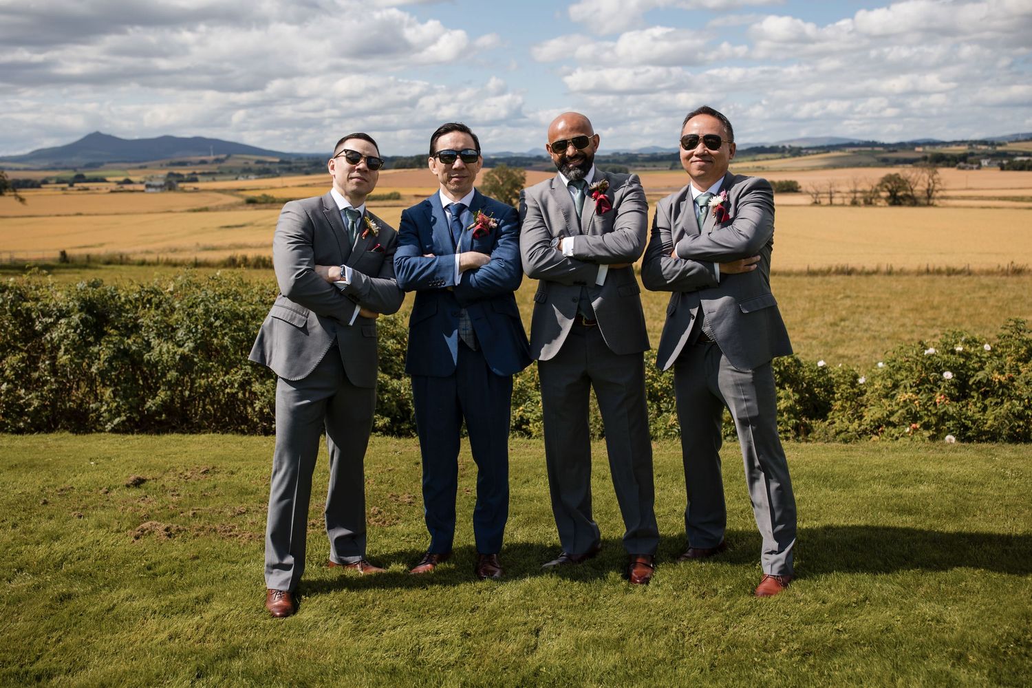 Group relaxes on grass overlooking scenic countryside with mountains and golden fields in distance.