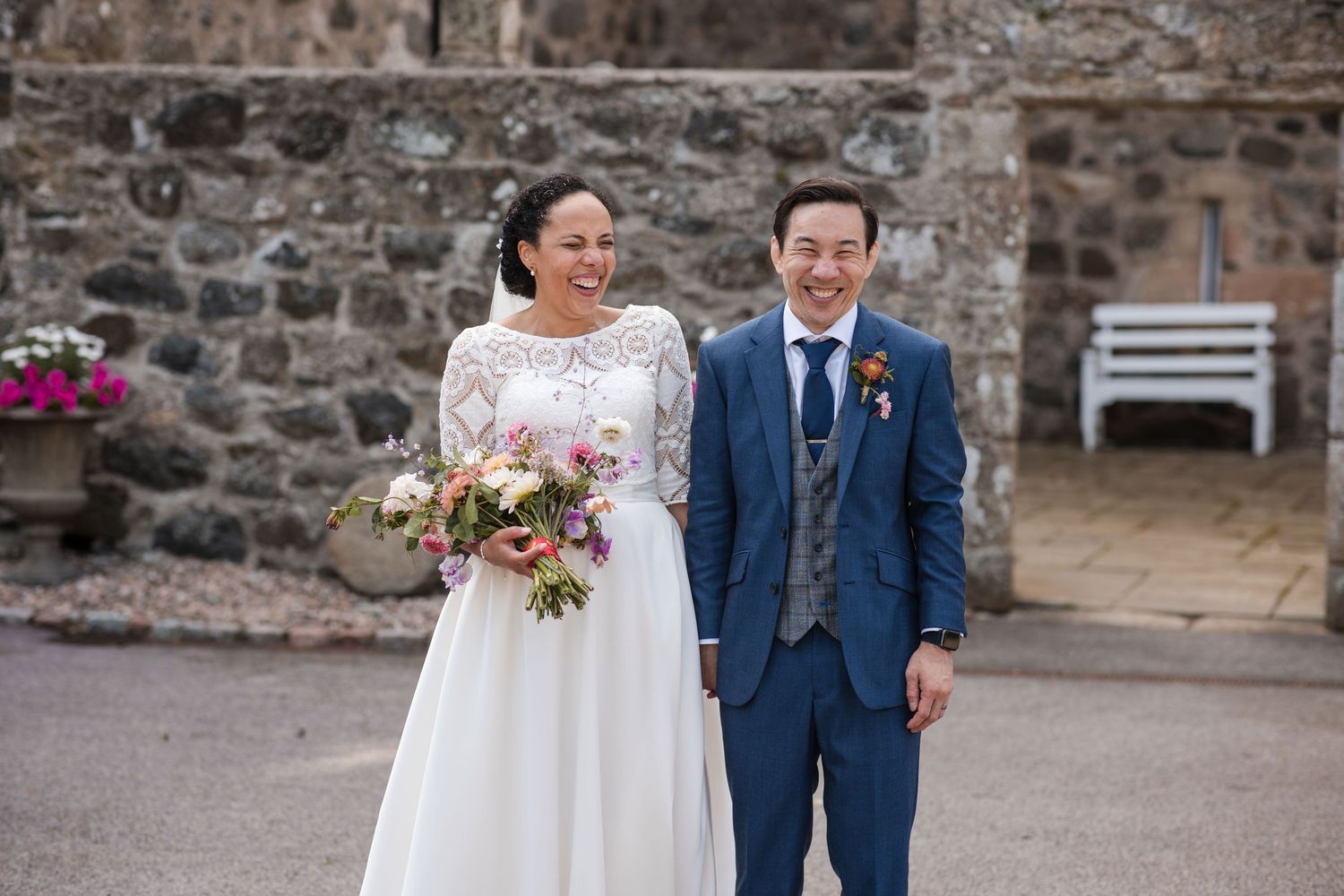 Wedding couple photographed against rustic stone wall backdrop.
