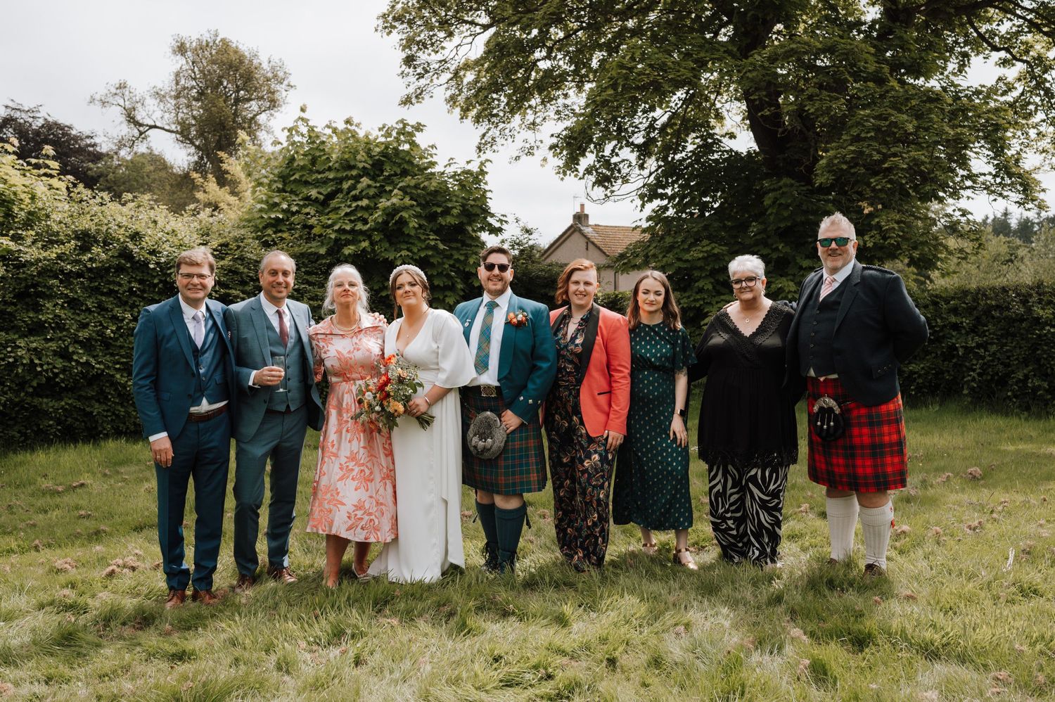 Wedding party in Scottish and formal attire poses together on lawn.