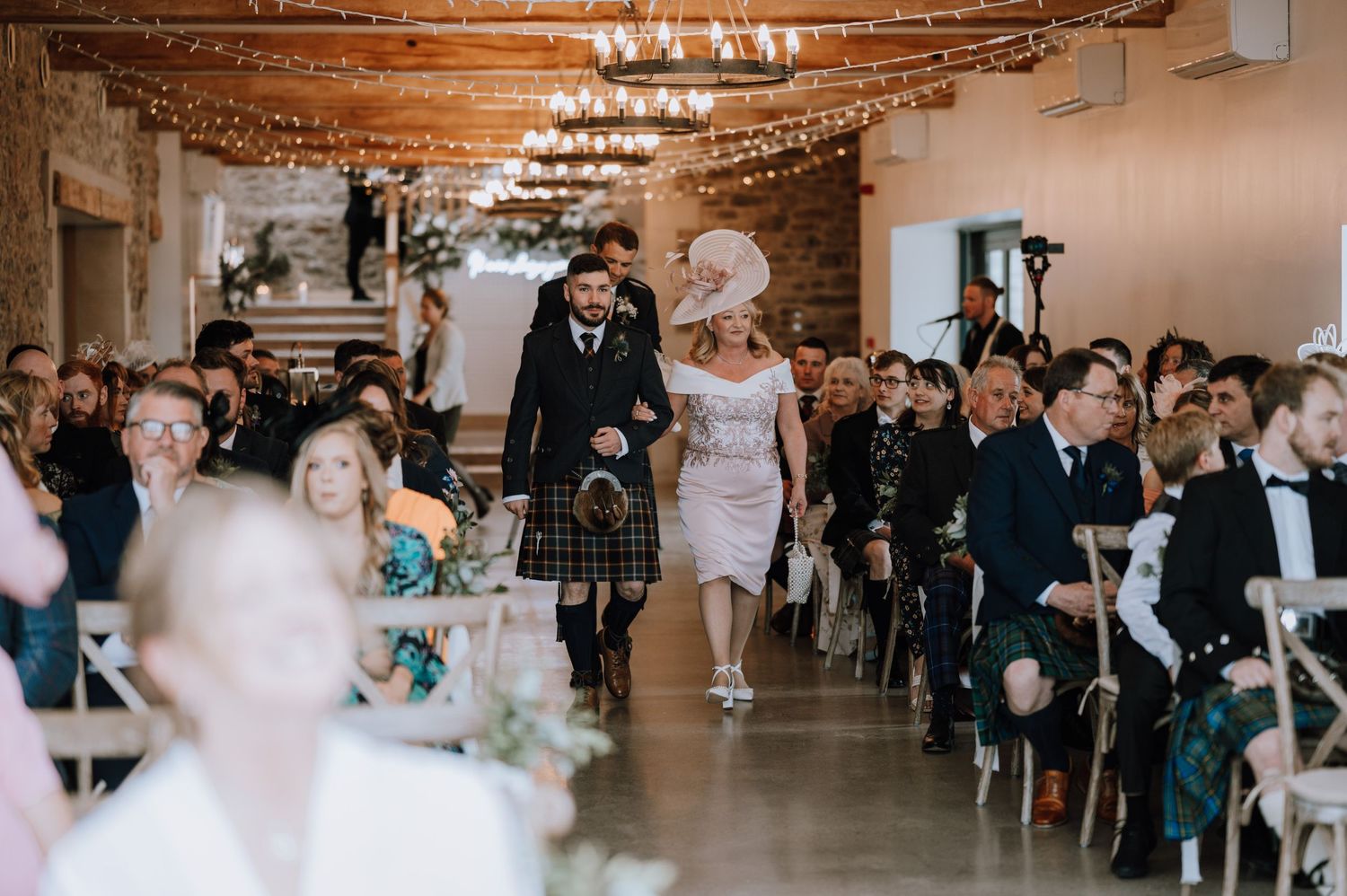 Wedding reception entrance in rustic venue with string lights and wooden beams overhead.
