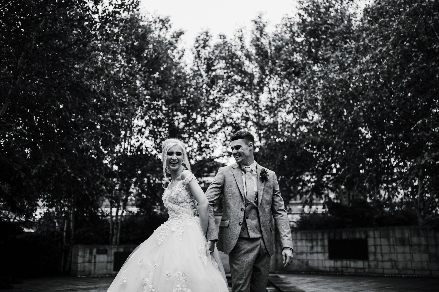 A black and white photo captures a wedding couple walking through a garden.