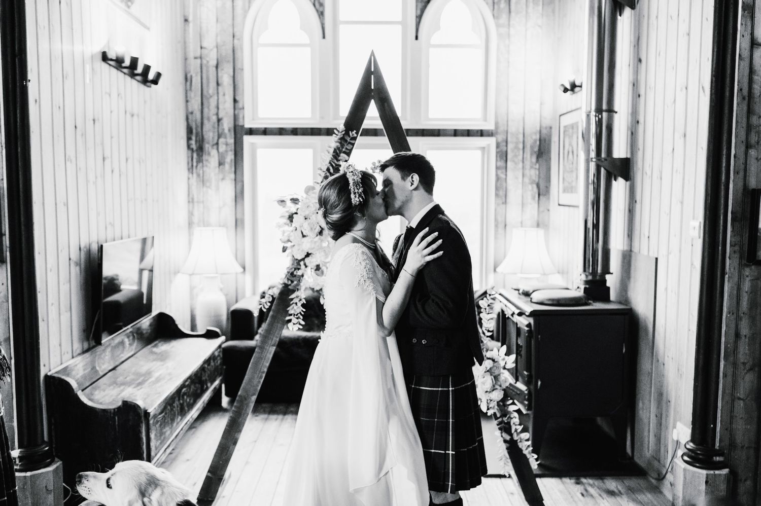 Black and white wedding photo captures intimate moment in front of chapel windows.