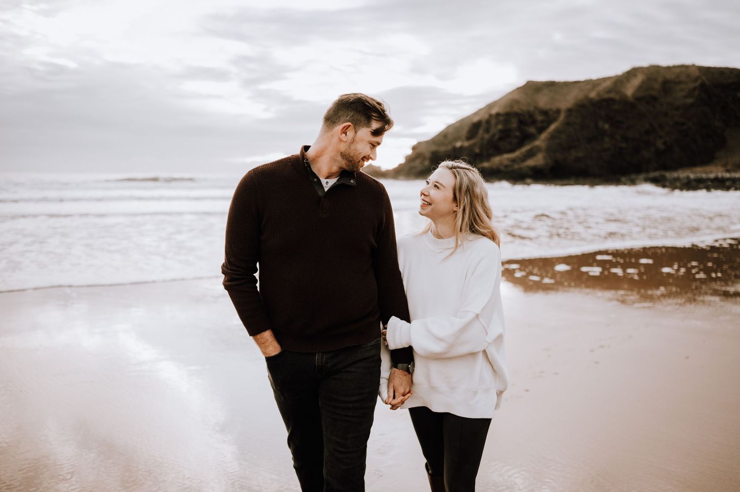 Happy couple walking together on a secluded beach with cliffs in the background.