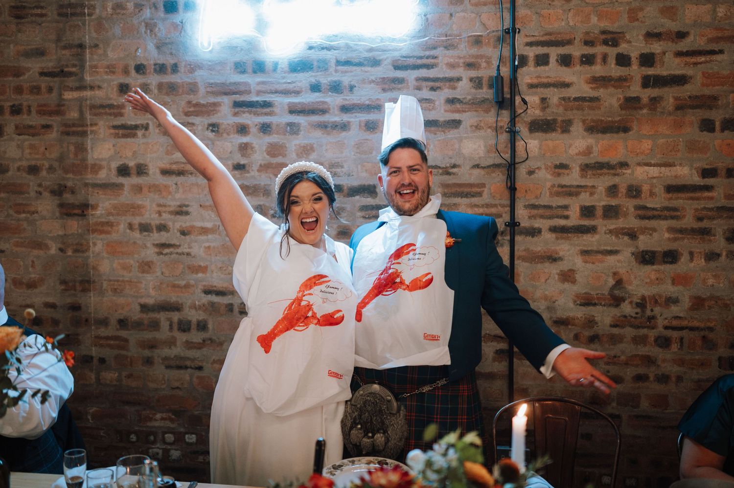 A couple in matching lobster shirts celebrates joyfully at their wedding reception.