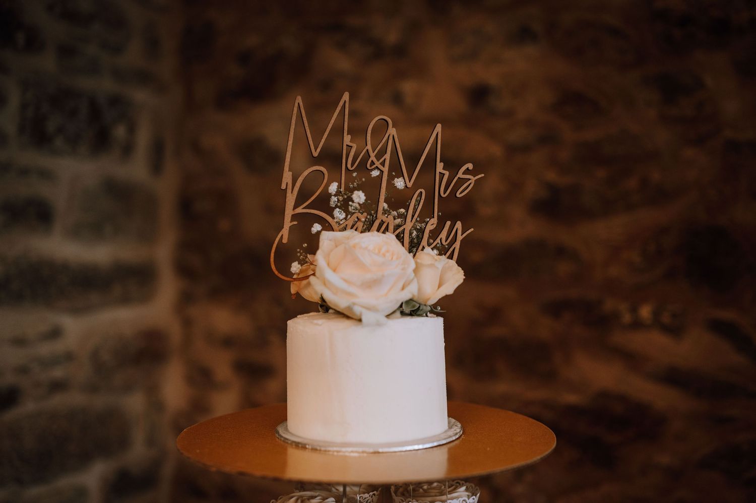 Close-up of elegant white wedding cake topper with gold 'Mr & Mrs' text and delicate floral decoration.