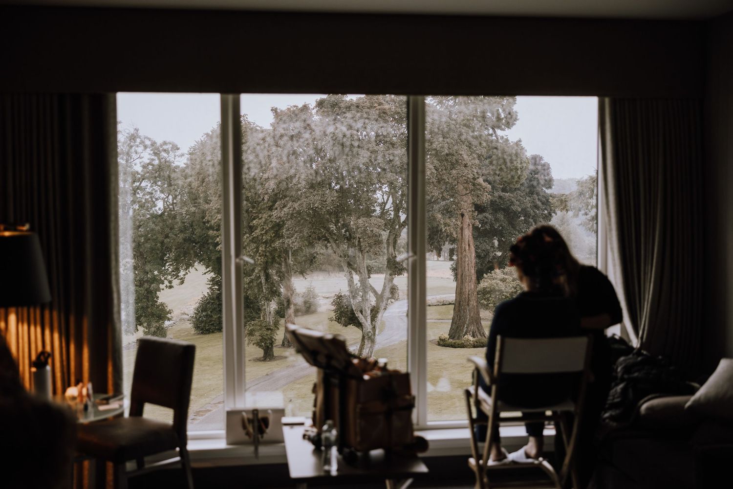 Silhouettes of people sit near large windows with trees visible outside.