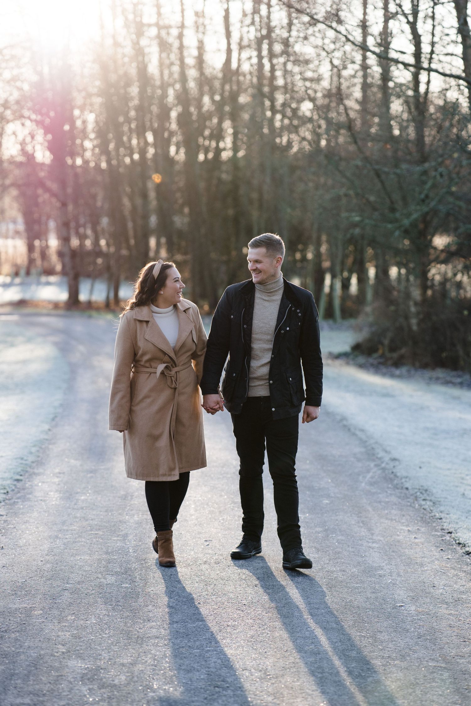 A couple takes a romantic winter walk along a frost-covered path at sunset.