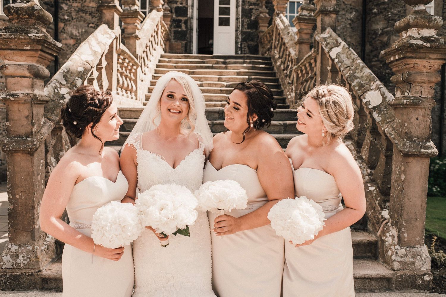 Wedding party poses elegantly on grand stone staircase with ornate architectural details.