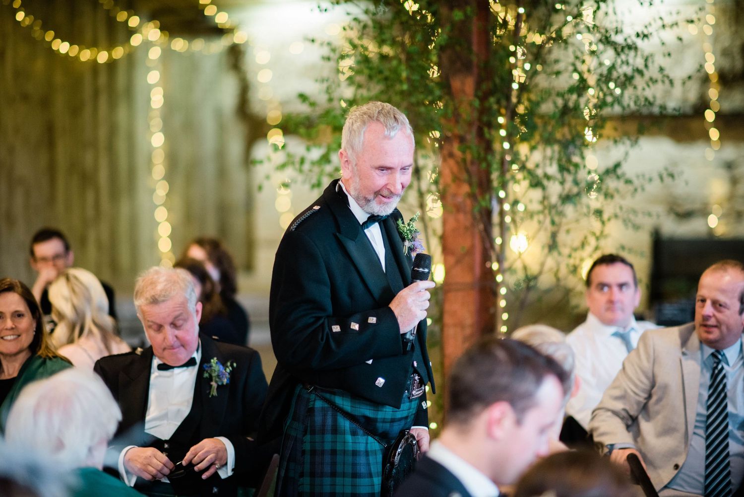 A Scottish wedding reception with guests gathered in a warmly lit rustic venue.