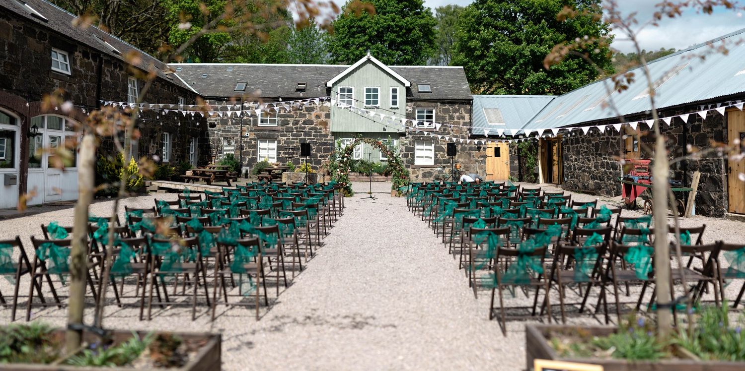 Outdoor wedding ceremony setup with teal chairs and string lights leading to a mint green house.