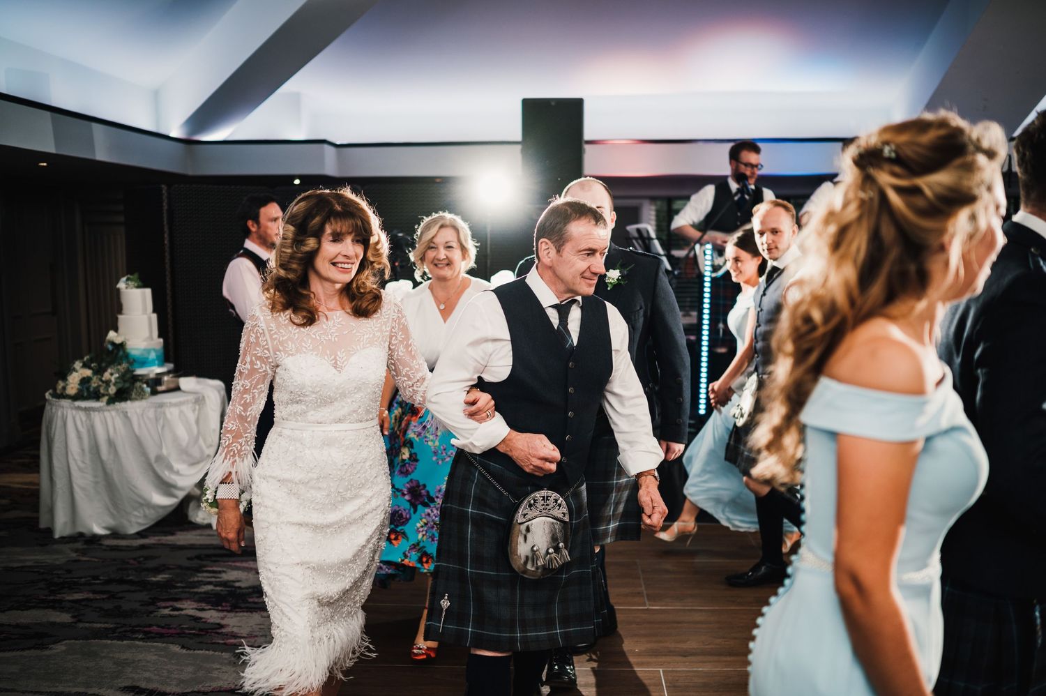 Wedding celebration on dance floor with people wearing kilts and formal attire.