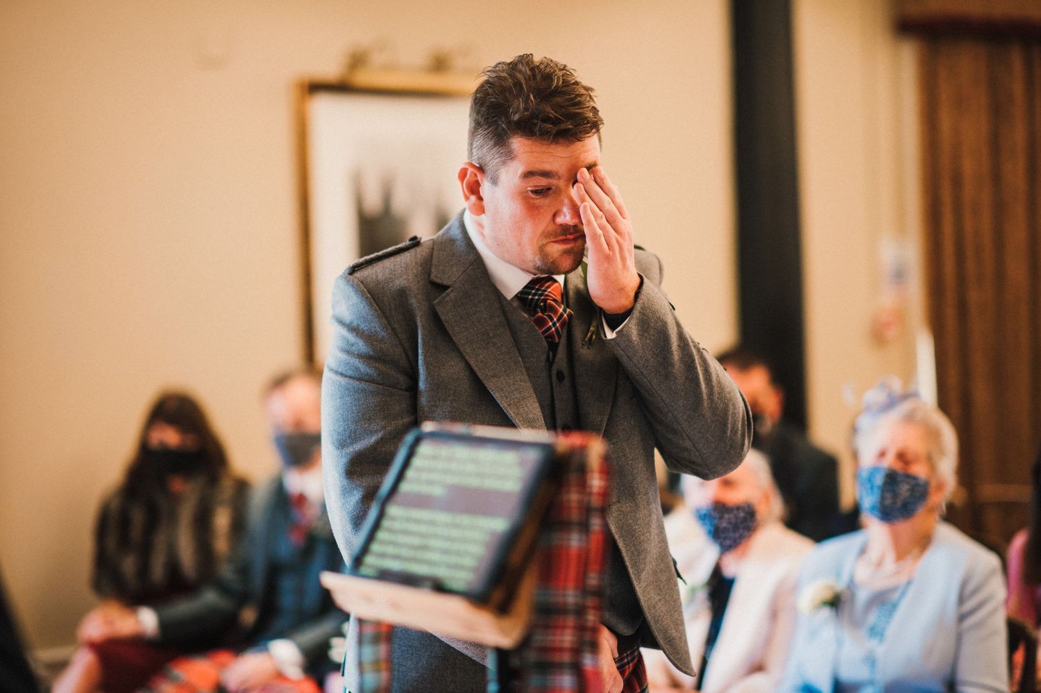An emotional moment captured during an indoor wedding ceremony with attendees wearing masks.