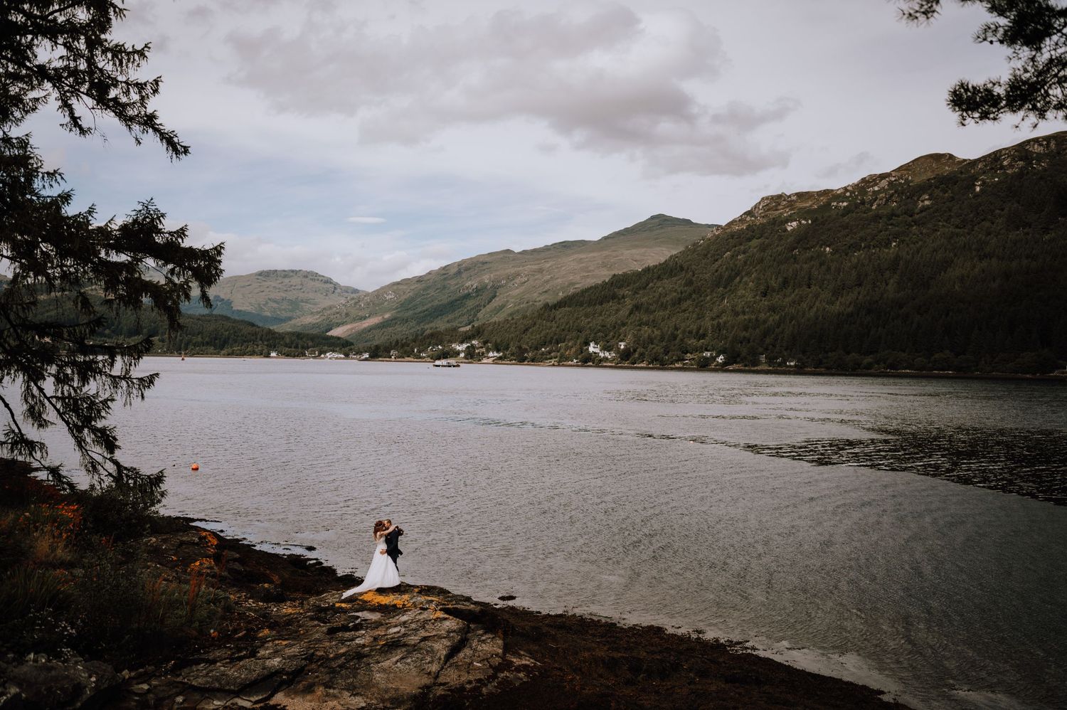 Dramatic aerial view of wedding ceremony site on cliffside overlooking mountain lake landscape.