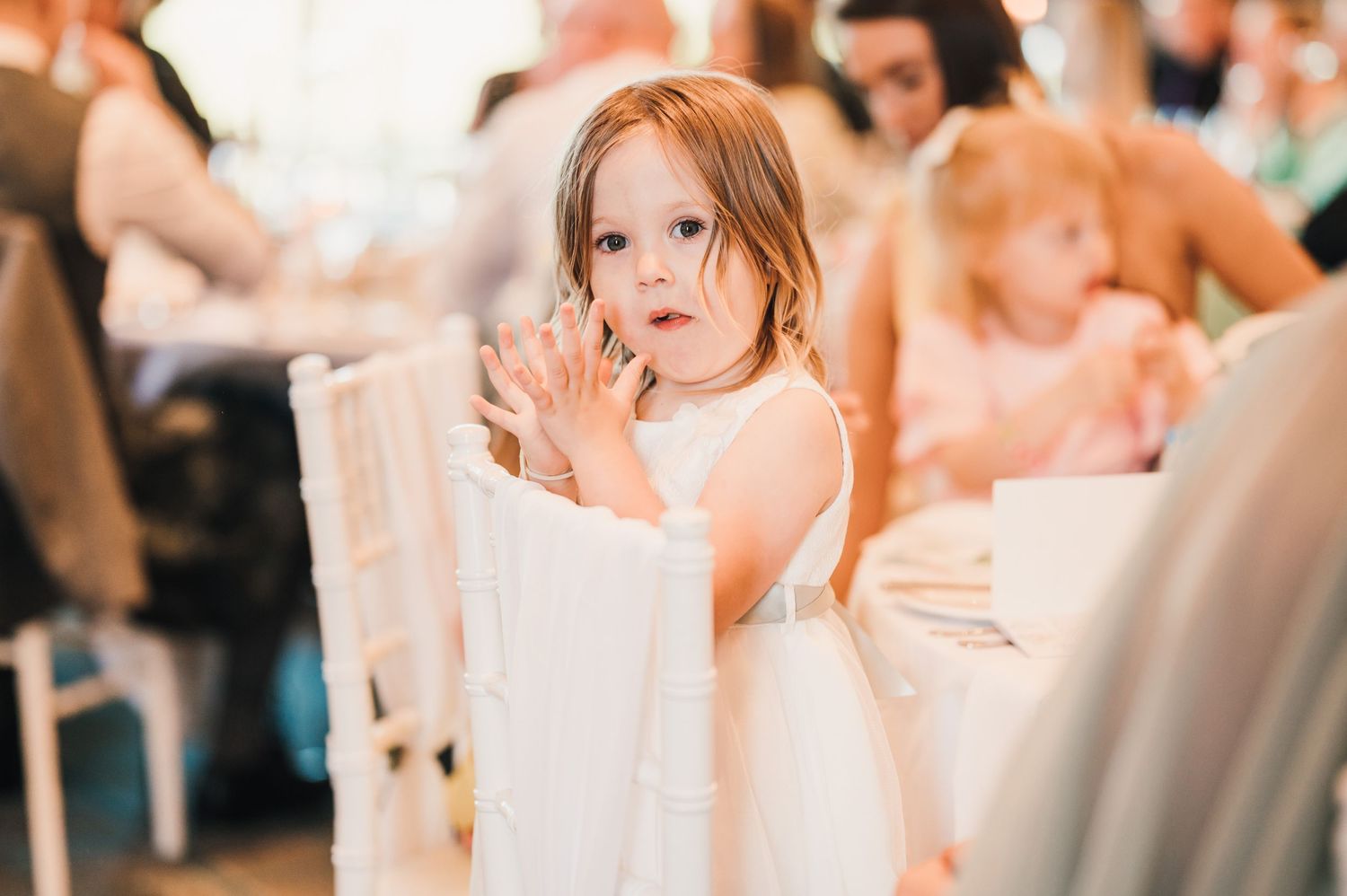 Young attendee in white dress enjoying festivities at wedding reception.