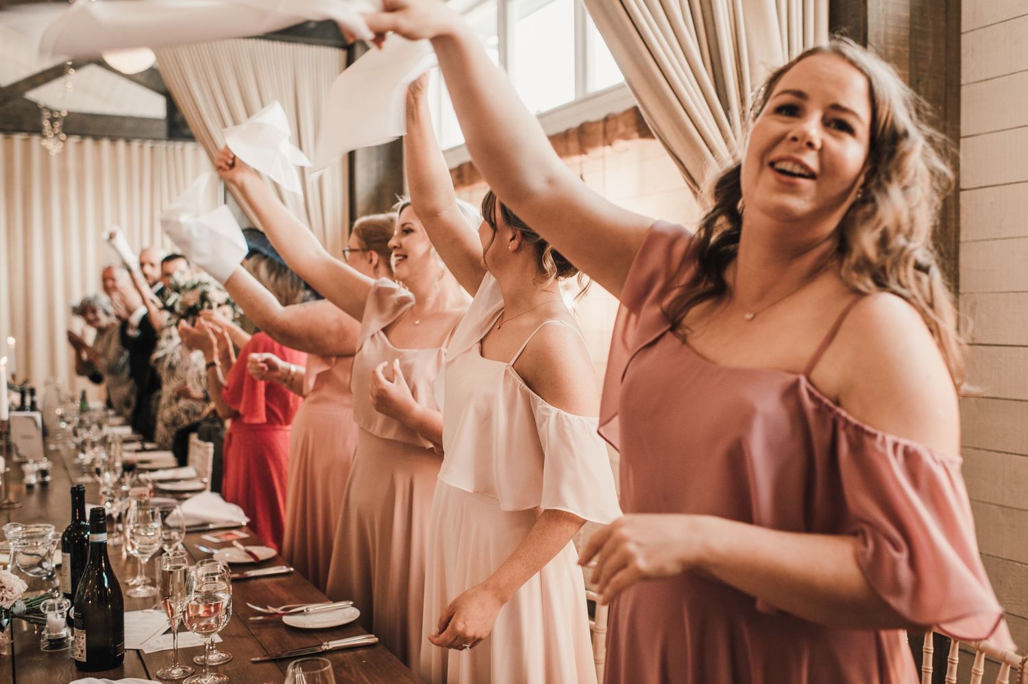 Wedding party celebrates at reception with coordinated dance moves in pink dresses.
