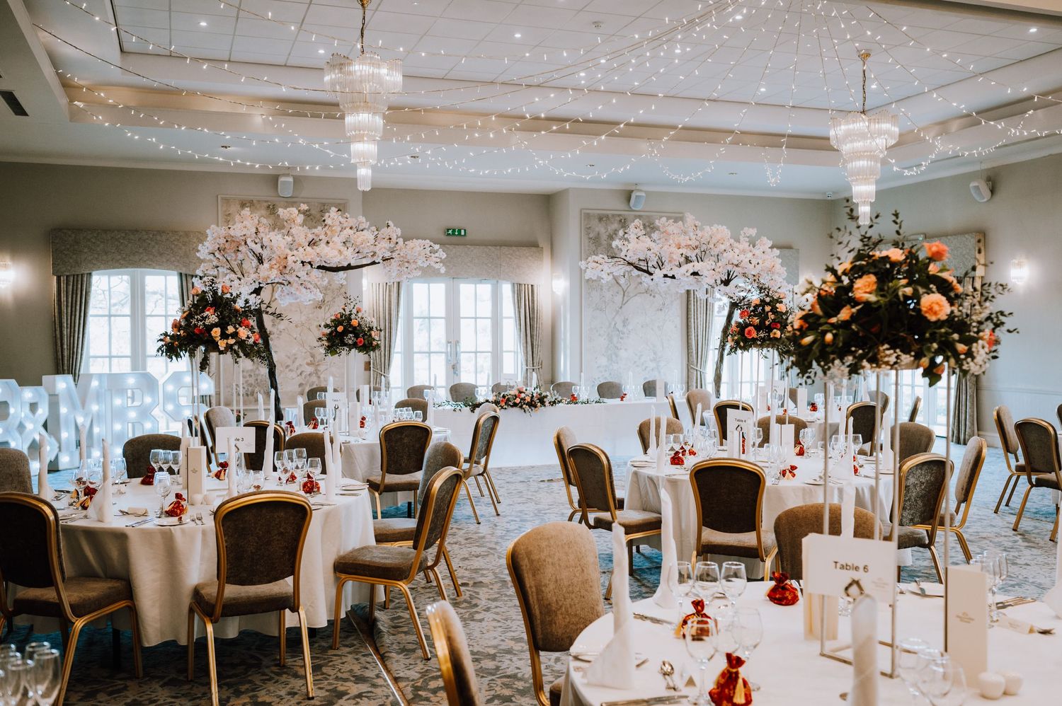 Elegant ballroom with cherry blossom trees and round tables set for a wedding reception.