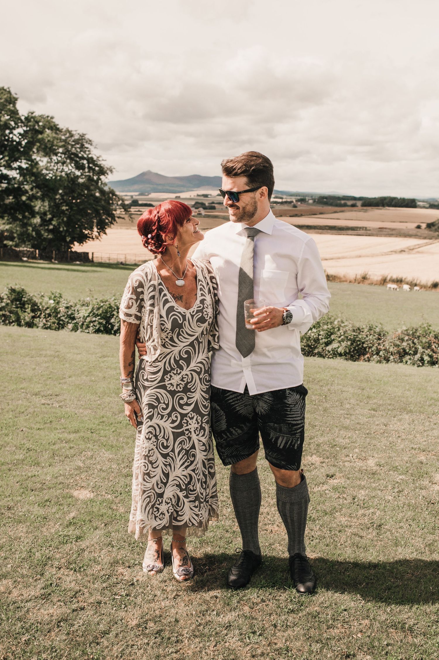 Couple enjoying moment together on grassy hilltop with scenic countryside views.
