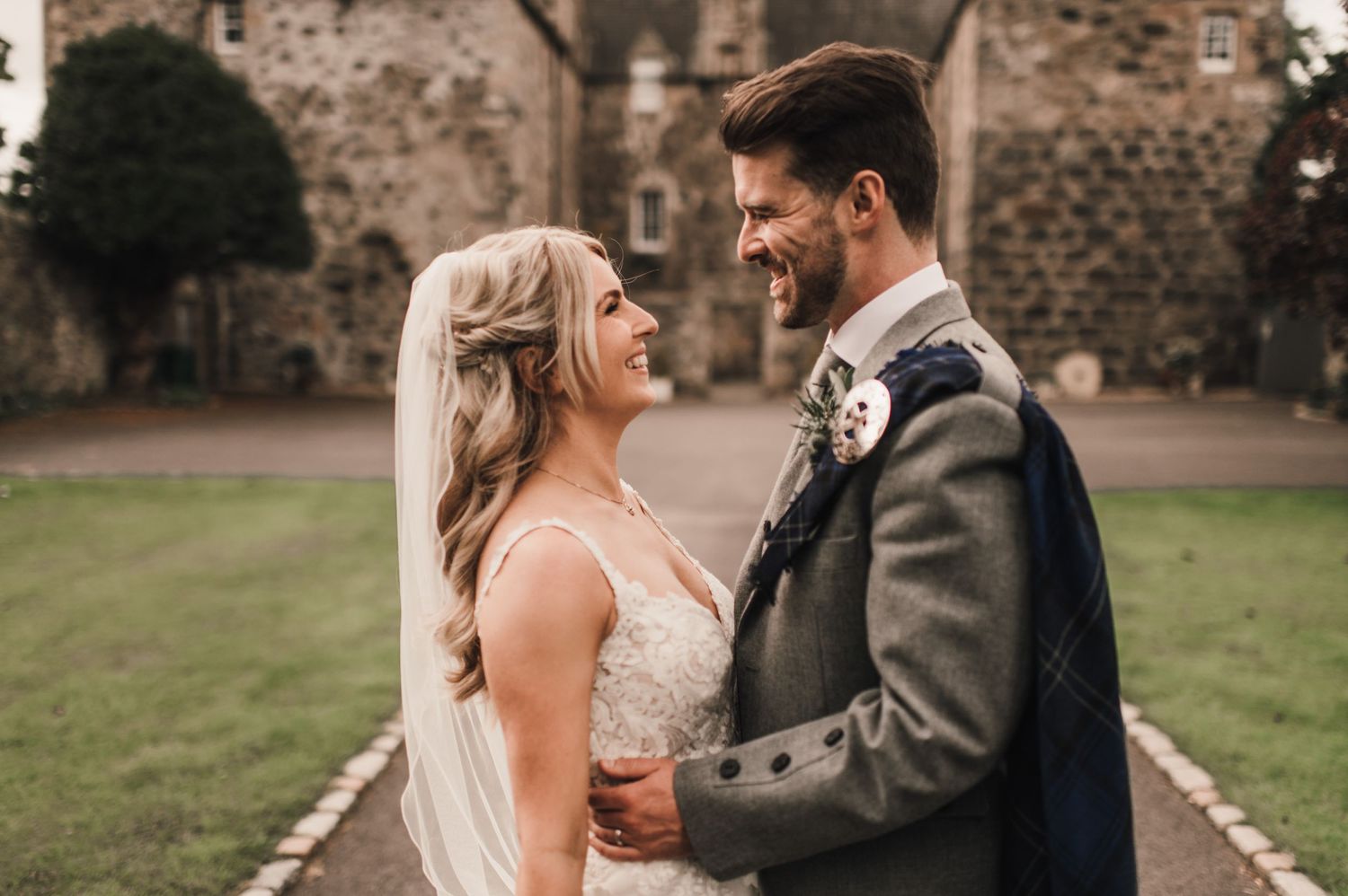 Romantic moment between couple in wedding attire with traditional Scottish elements against stone castle backdrop.