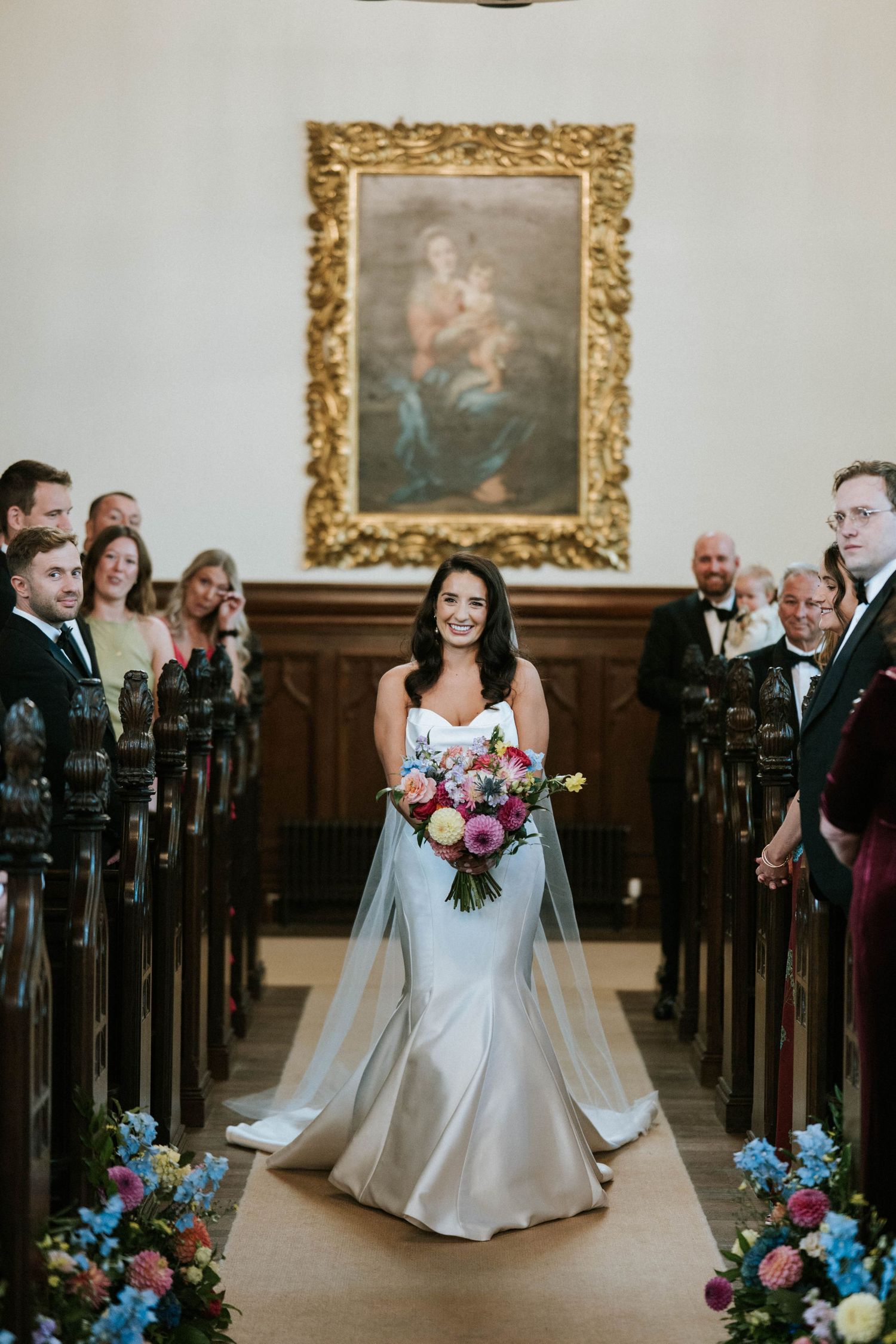 A wedding ceremony in progress inside an elegant hall with wooden pews and gold-framed artwork.