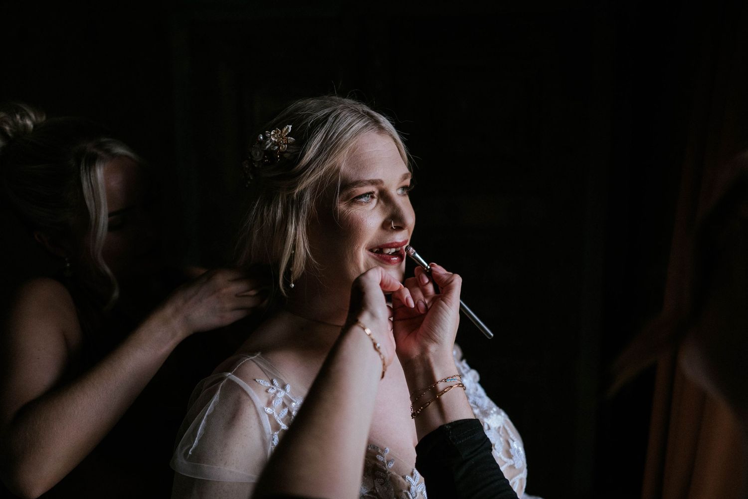A delicate bridal preparation moment captured in dramatic low-key lighting with soft focus.