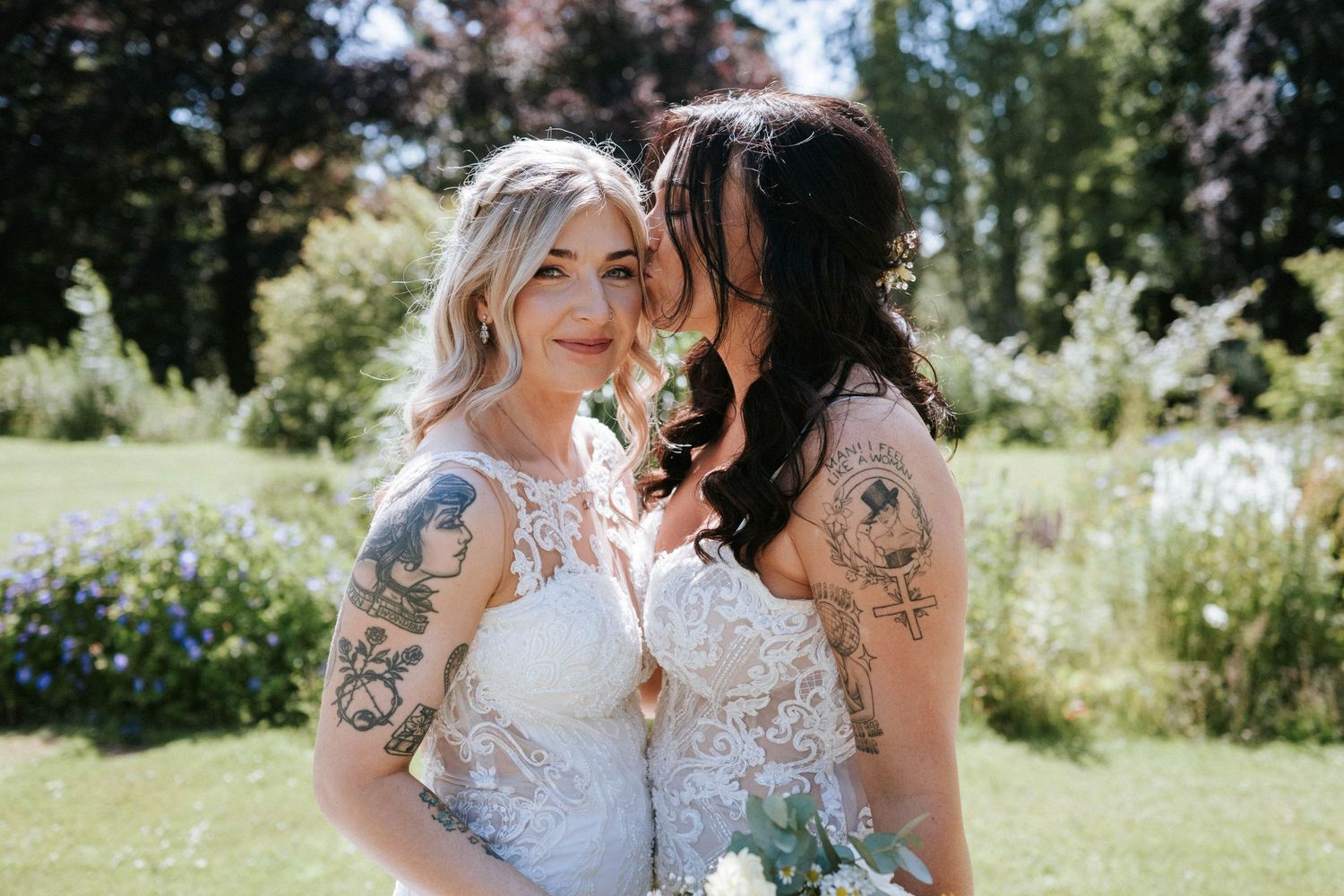 Wedding couple embraces while standing in a sunny outdoor garden with trees.