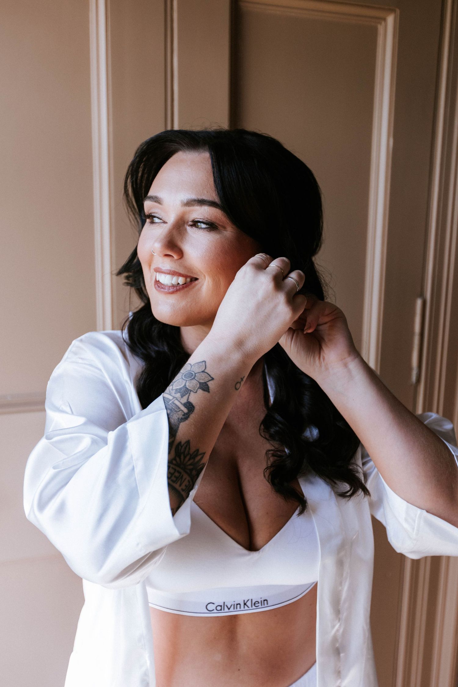 A woman in white loungewear and robe adjusts her hair while getting ready.