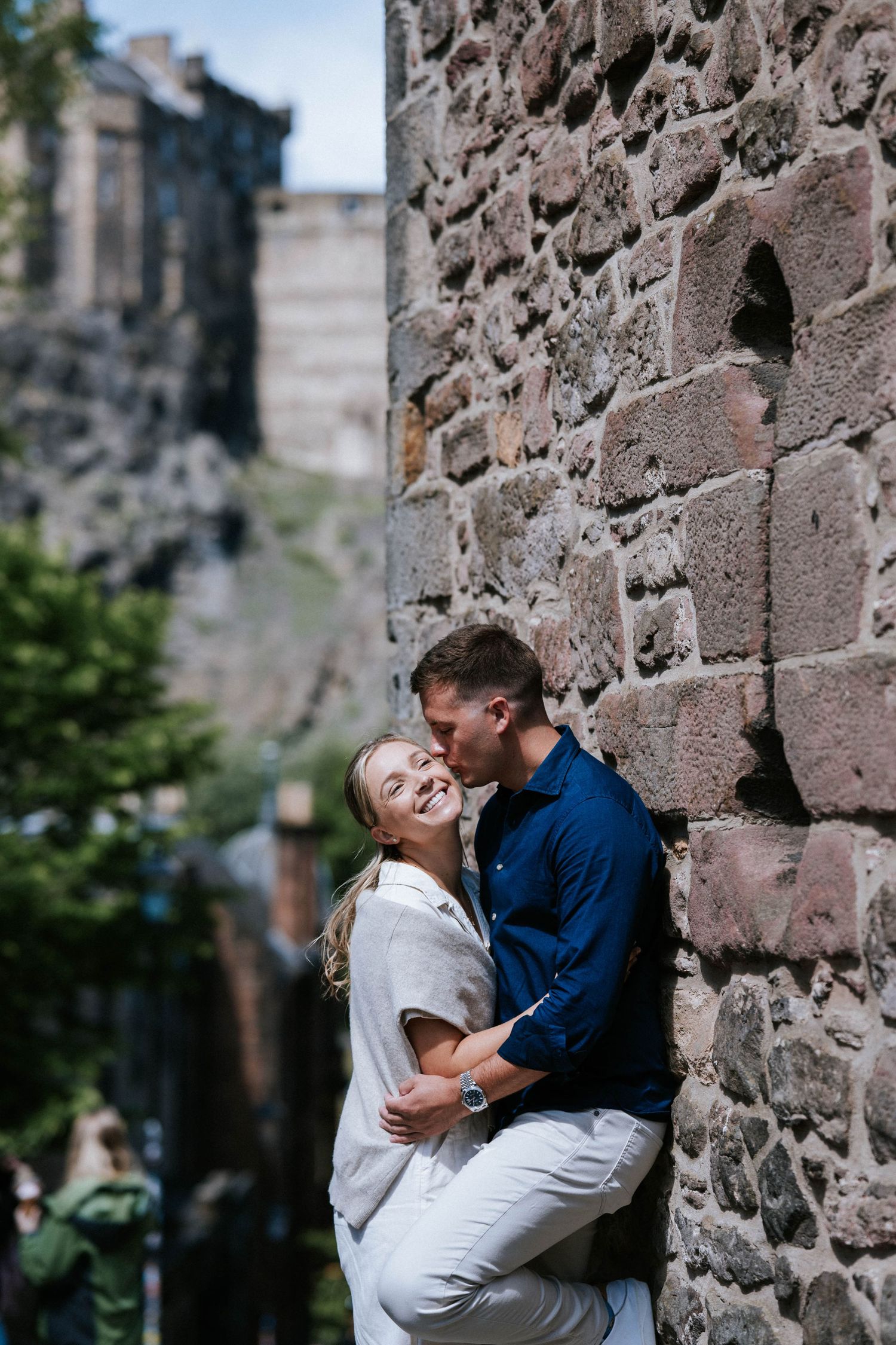 Engagement photography session Aberdeen. A romantic couple embraces against a rustic stone wall backdrop.