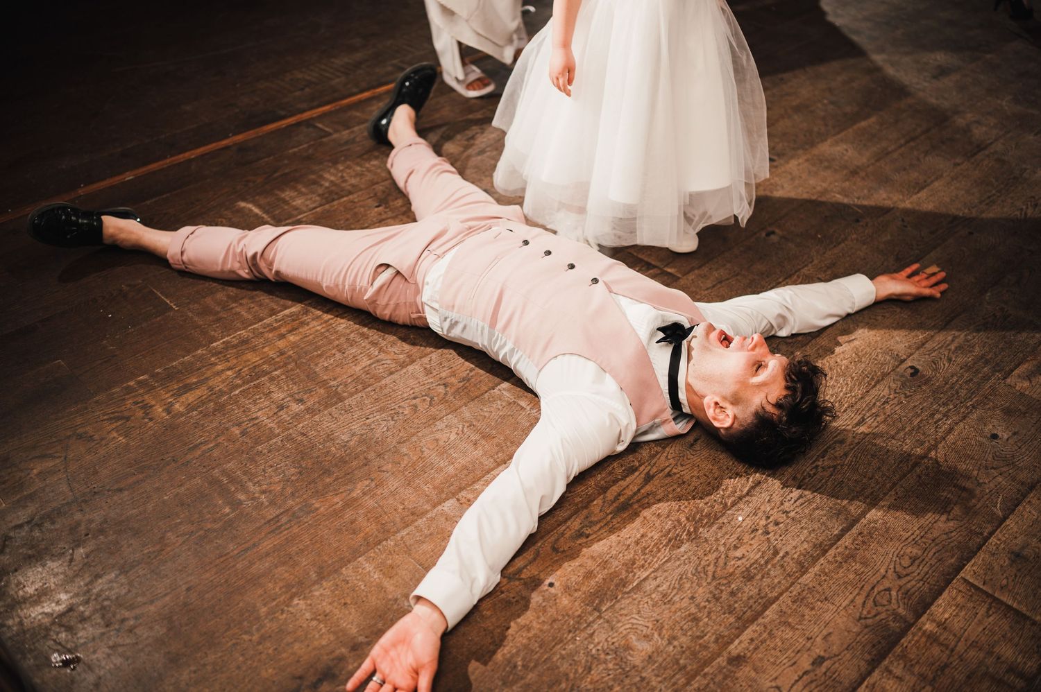 Logie House Wedding Photography. Wedding guests lying on wooden dance floor in playful poses during reception celebration.