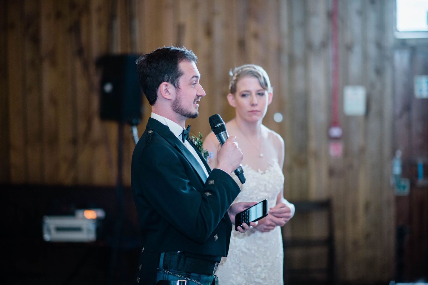 Couple sharing a moment during wedding speeches in rustic wooden venue.
