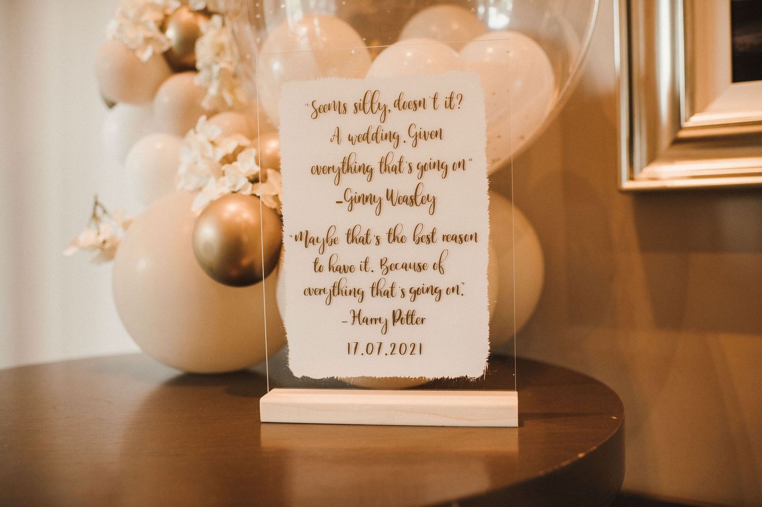 Romantic wedding quote displayed on white stand with gold balloons and decor.