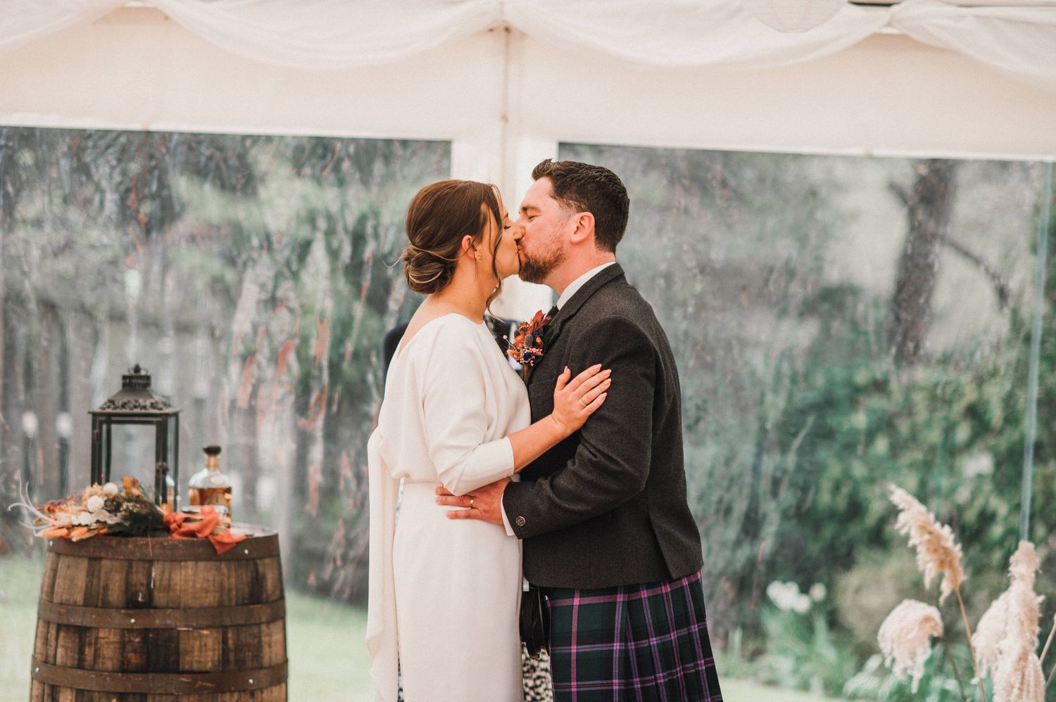 Couple sharing intimate moment during wedding ceremony under white tent with rustic decor.