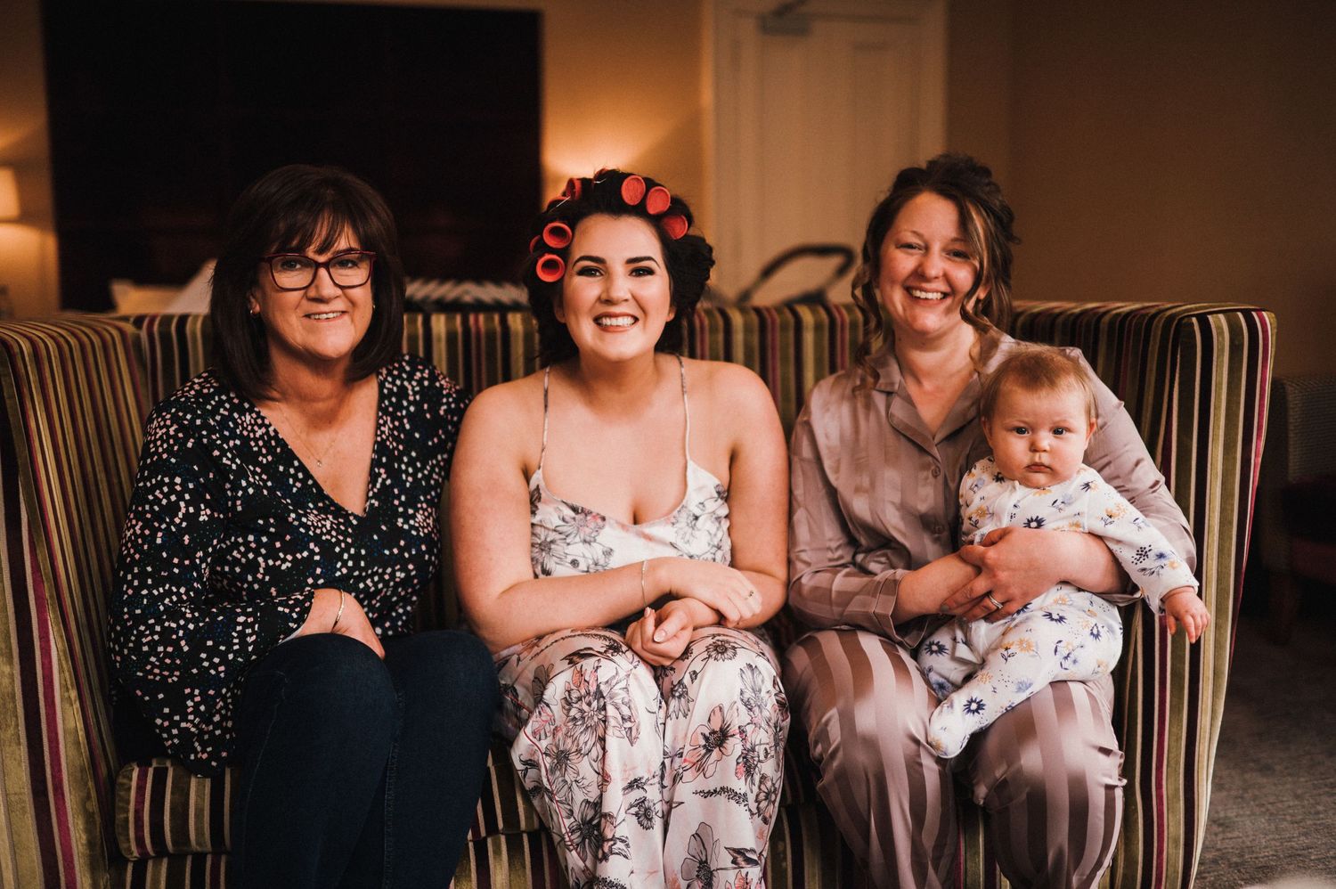 Multi-generational family gathering on striped couch during wedding preparations.