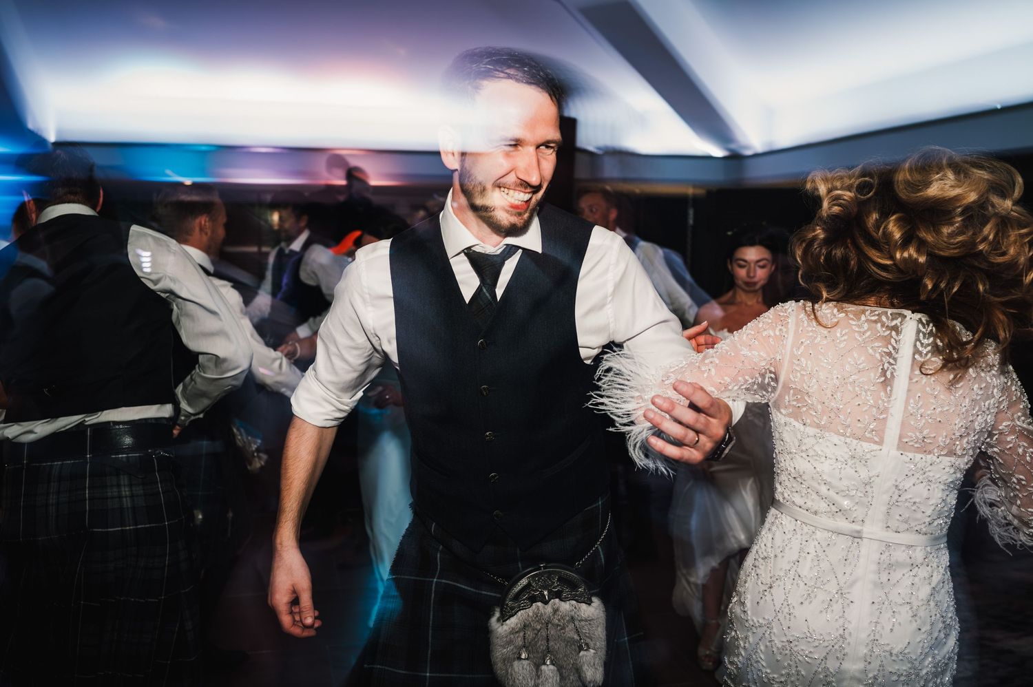 Wedding celebration on dance floor with guests in evening attire.