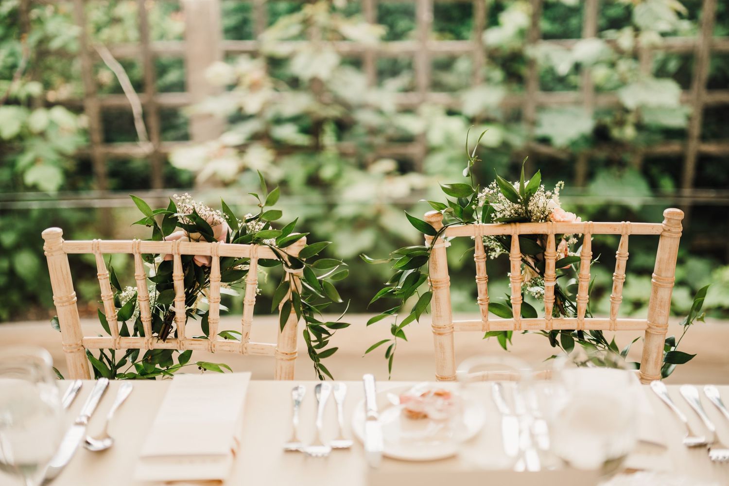 Rustic wooden chairs decorated with greenery garlands at wedding reception.