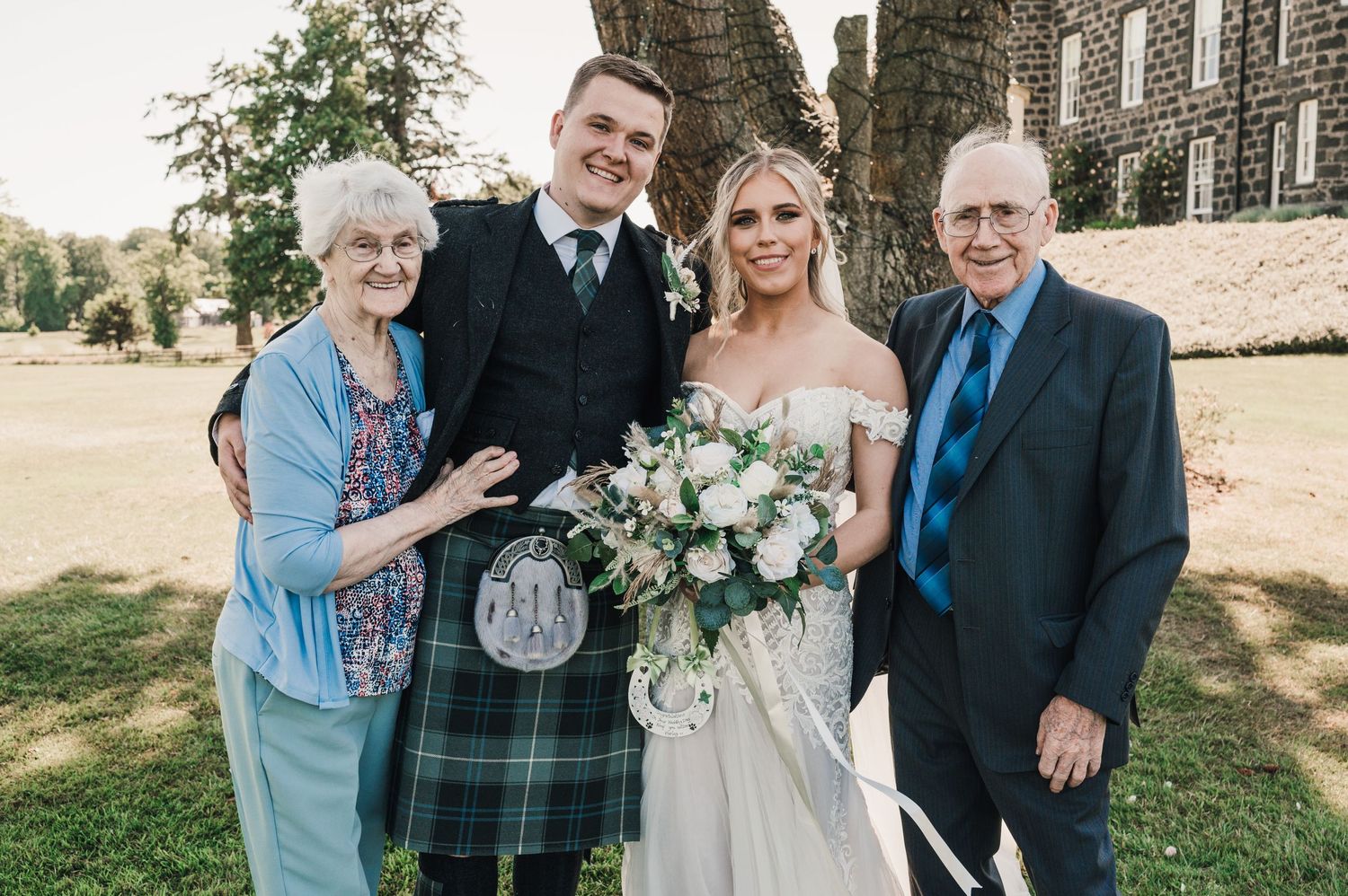 A formal wedding portrait with four people in front of a stone church.