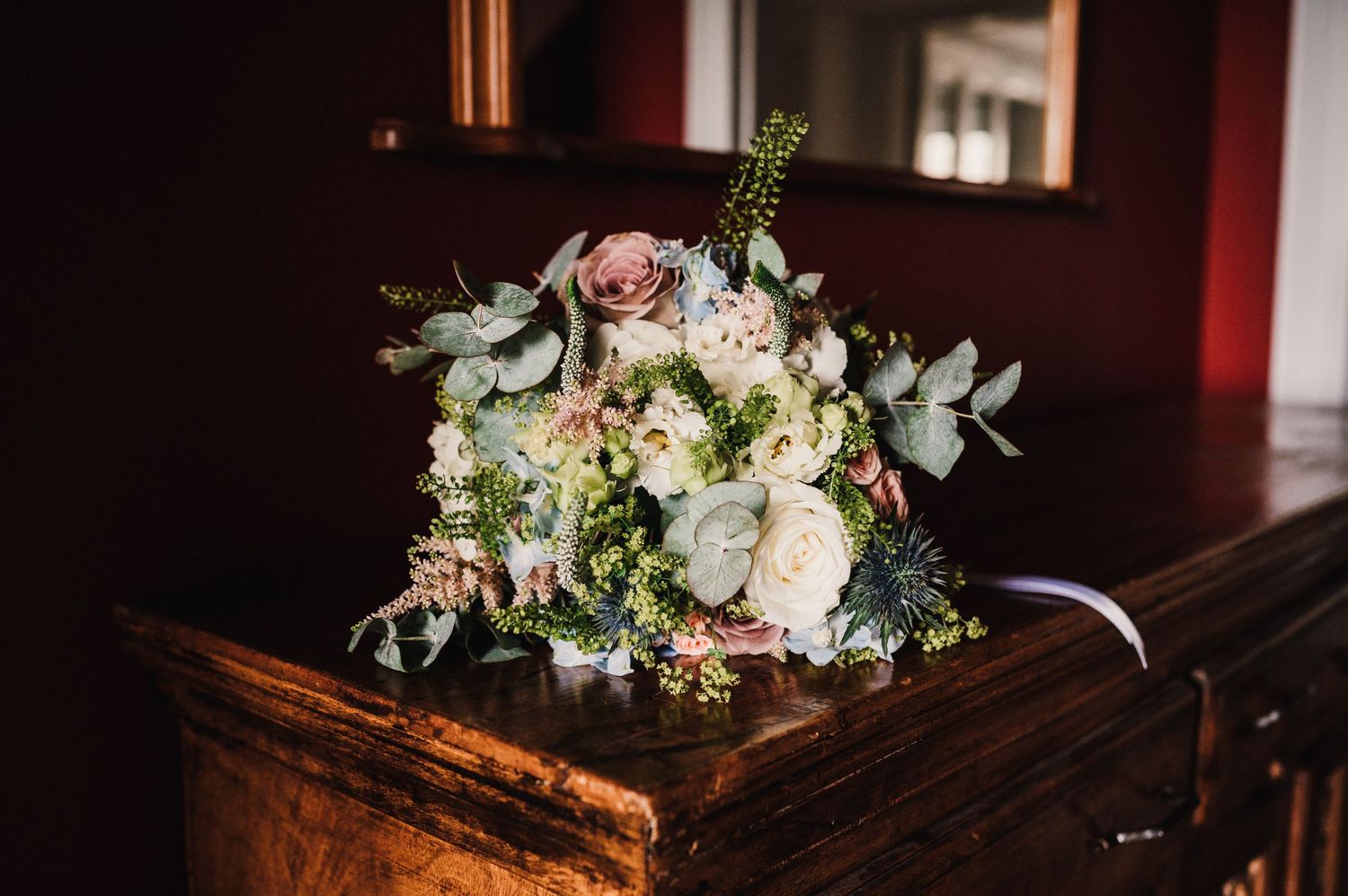 A romantic bridal bouquet with pink roses, eucalyptus and mixed flowers on a wooden surface.