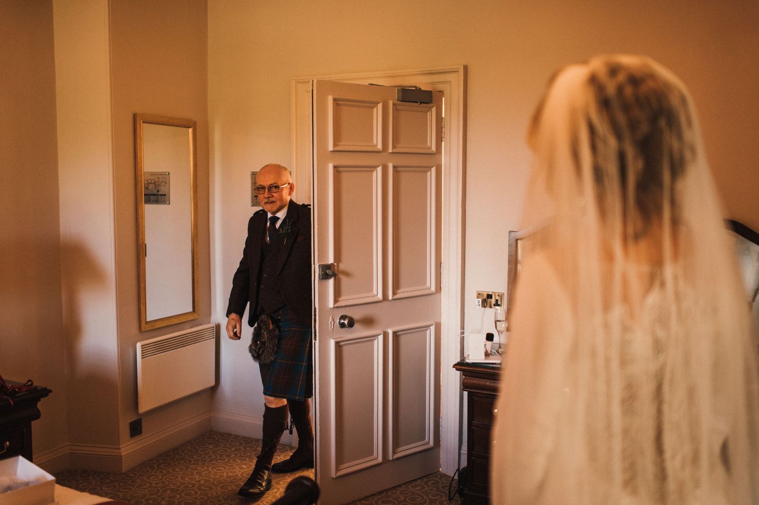 Emotional first look moment through doorway in warm lighting.