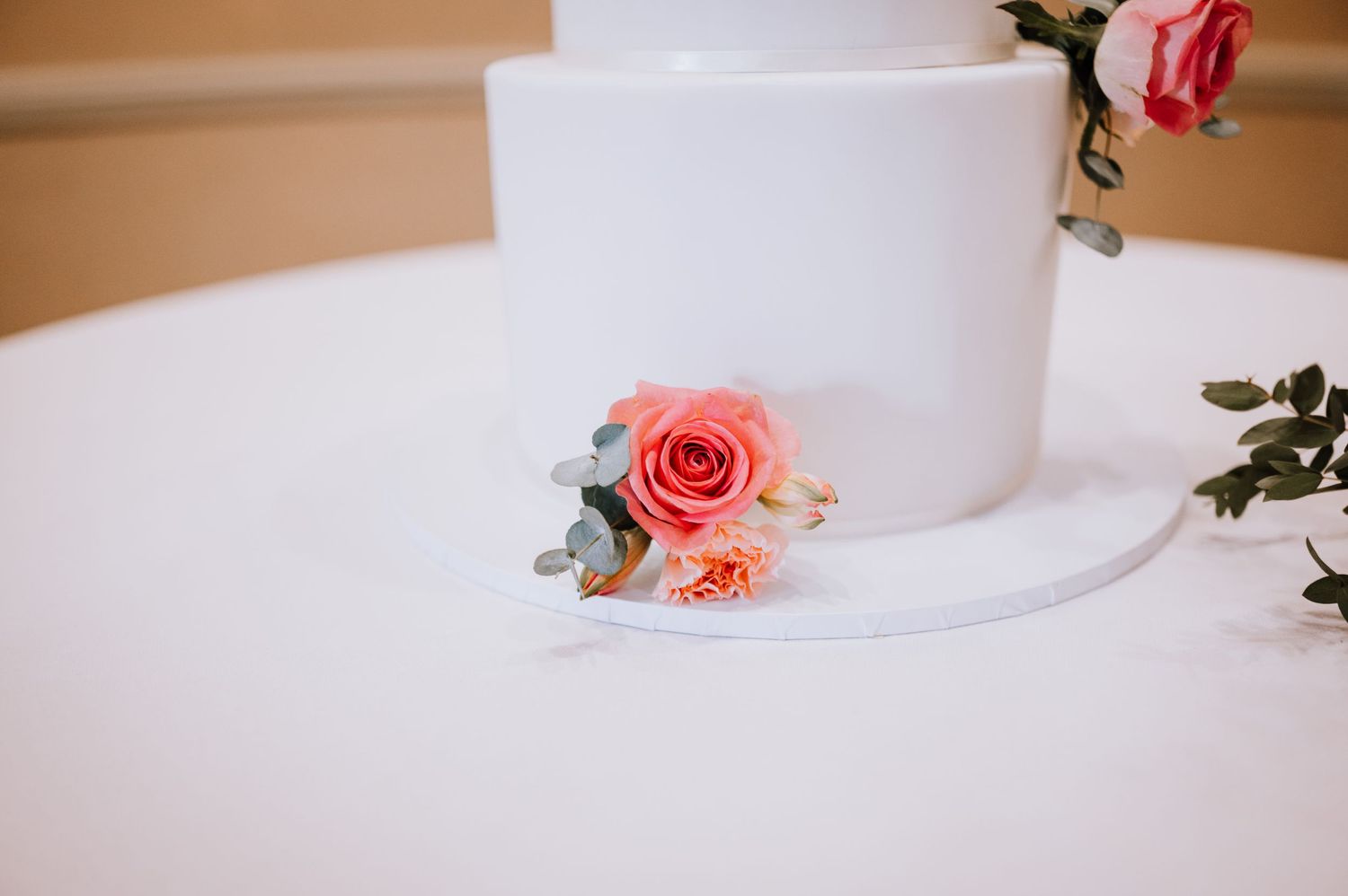 Minimalist white wedding cake adorned with a single coral rose and greenery.