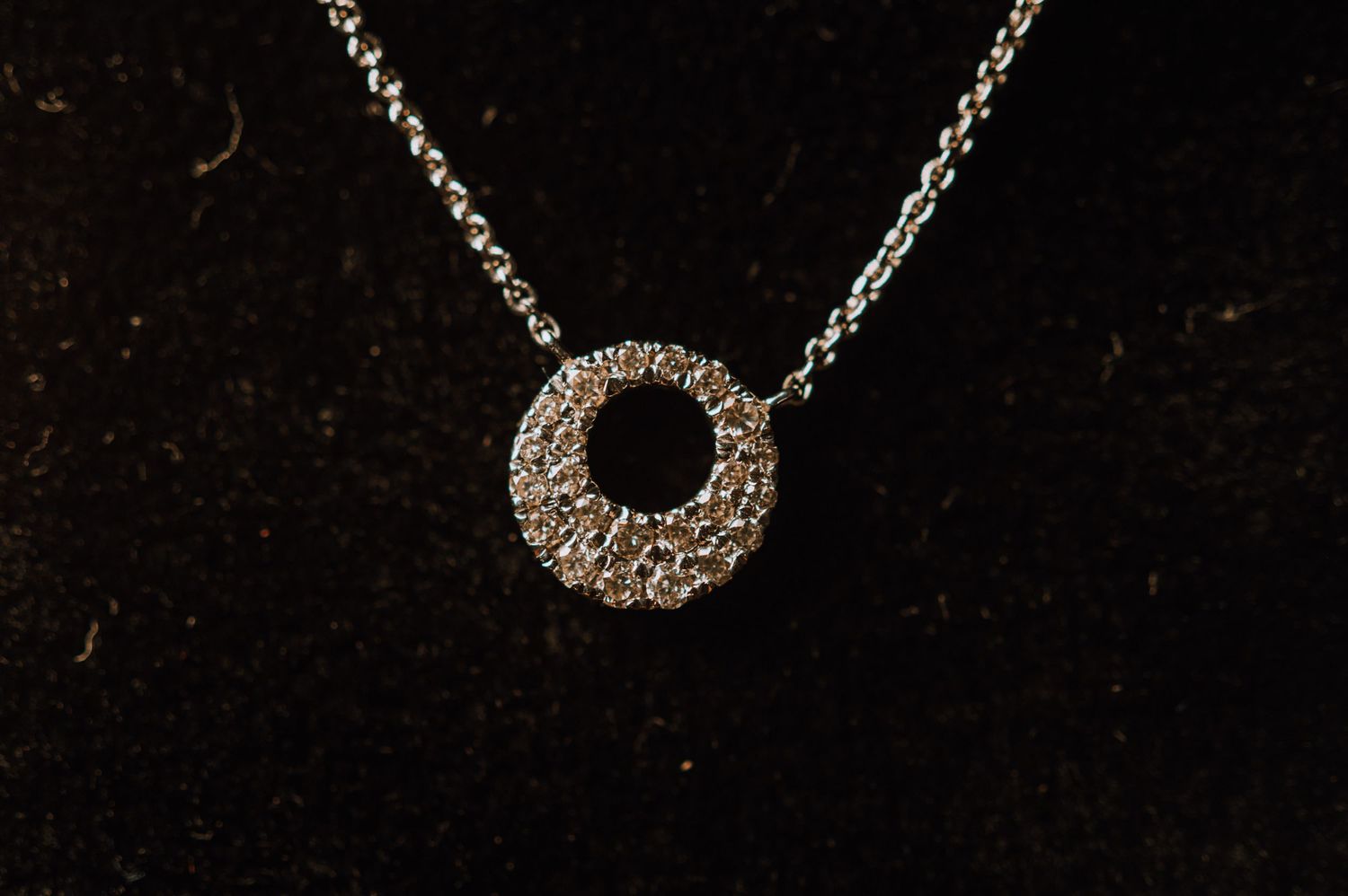 A delicate silver circular pendant necklace with rhinestone details on a dark background.