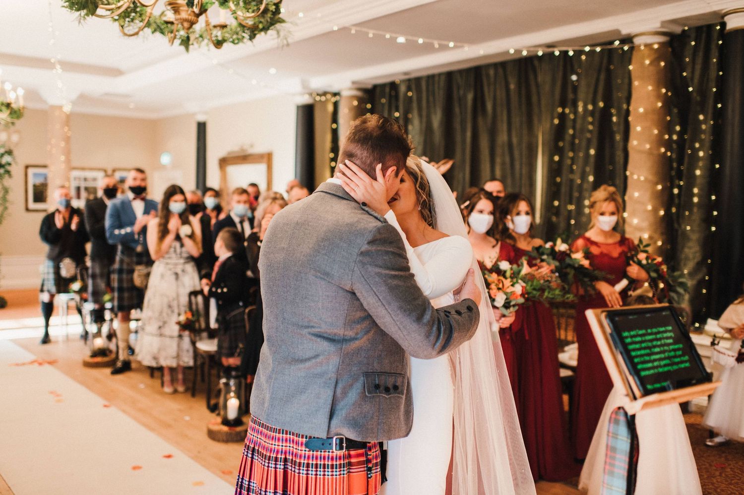 A Scottish wedding ceremony shows the first kiss in an elegant venue decorated with fairy lights.