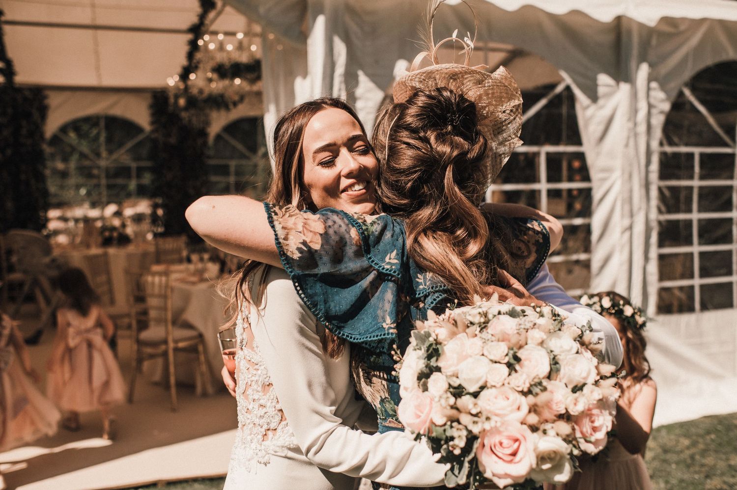 Two people share an emotional embrace at a wedding reception with pink floral bouquet.