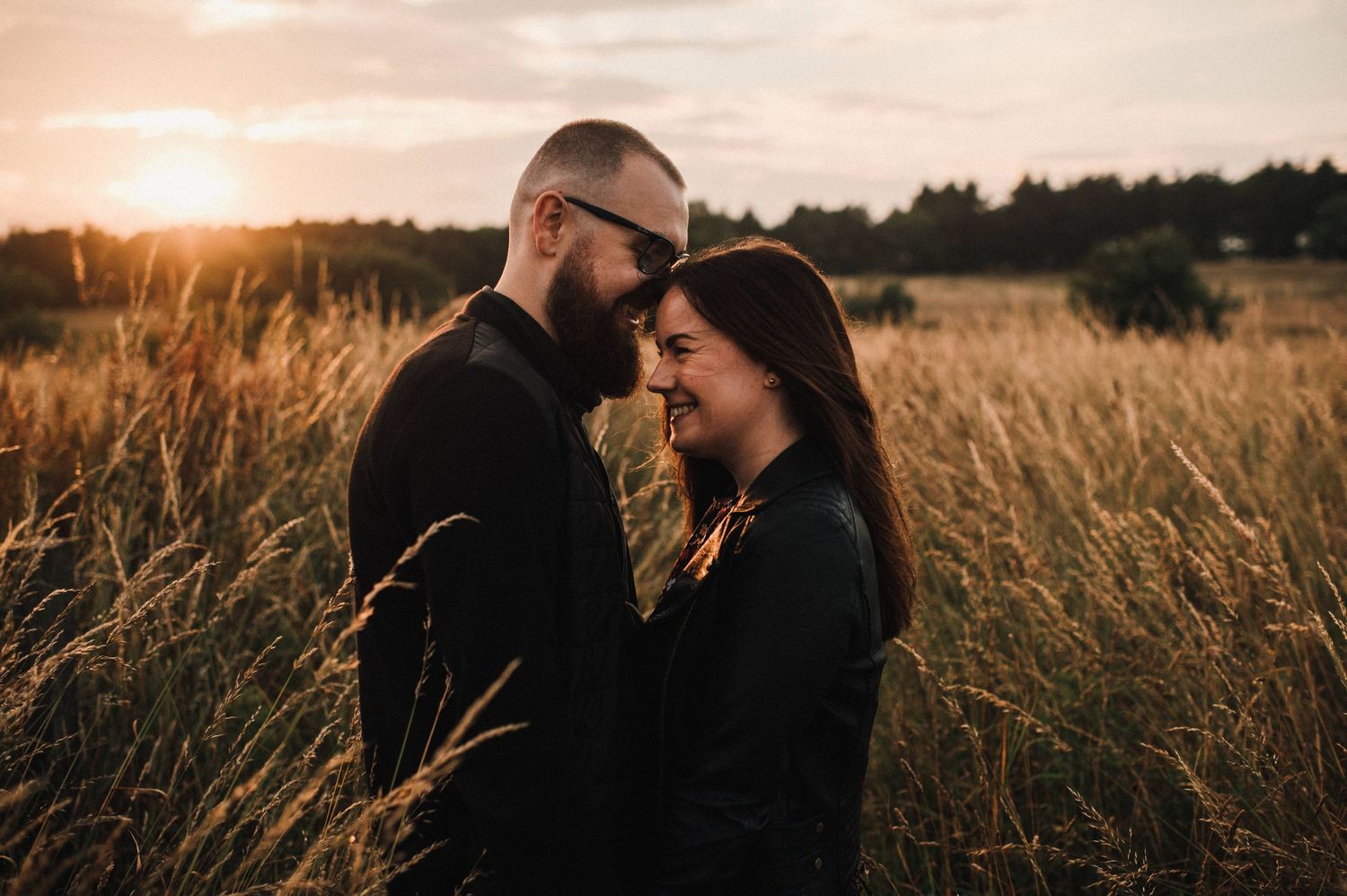 A tender embrace captured in a field of tall grass with warm sunset lighting.