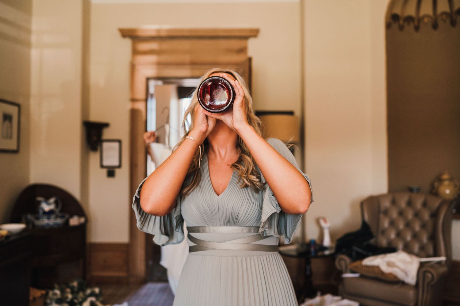 Someone in a flowing sage dress takes a big drink from a beverage can.