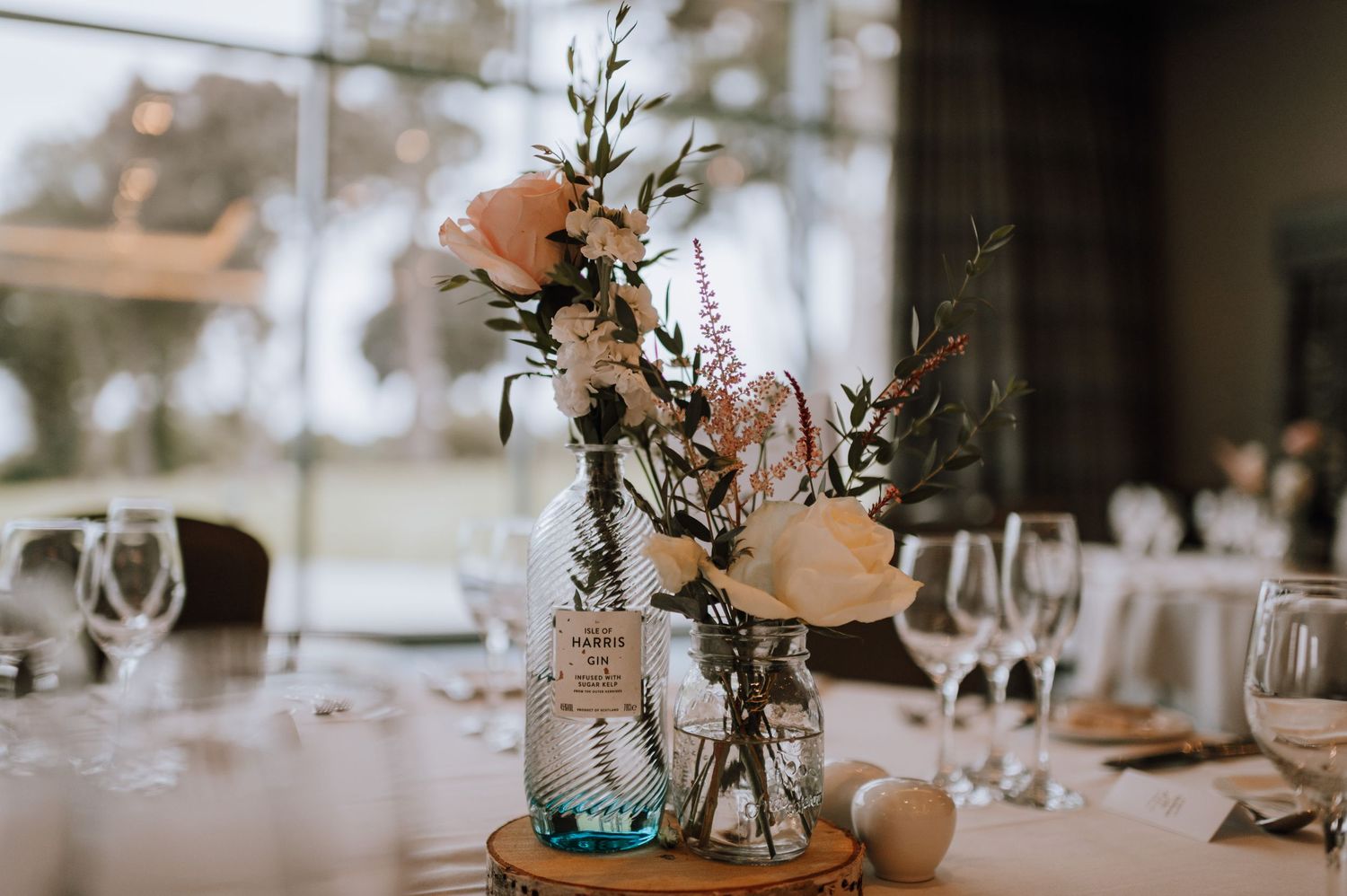 Elegant wedding centerpiece with peach roses and branches in mason jar on wooden slice.