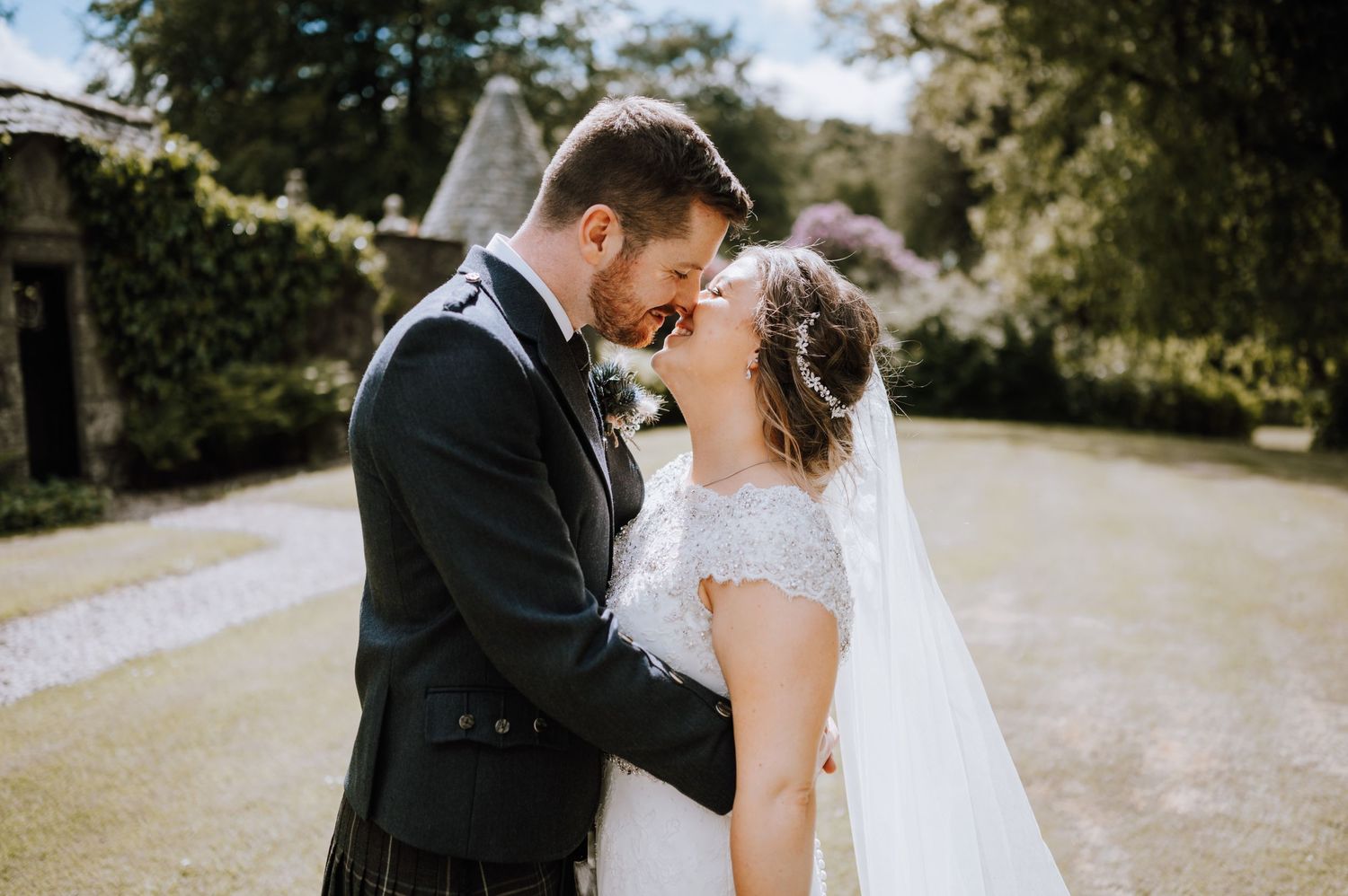 A romantic wedding couple share an intimate kiss on a garden path in soft natural lighting.