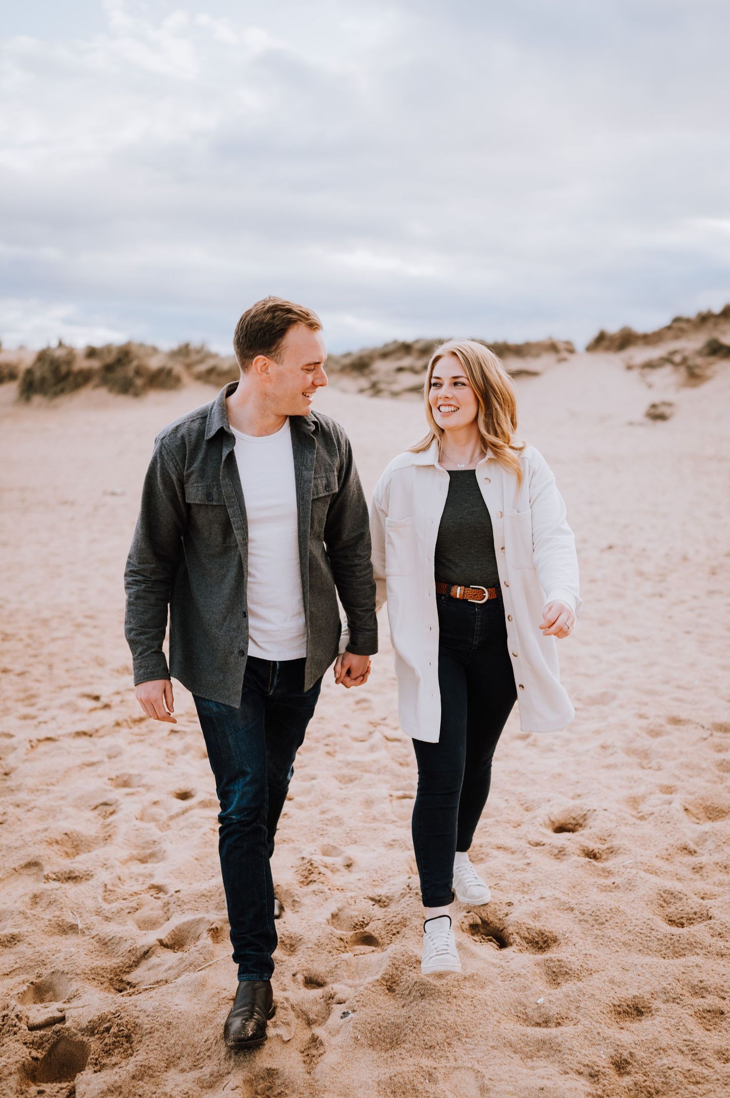 Happy couple walking together on sandy beach during overcast day.