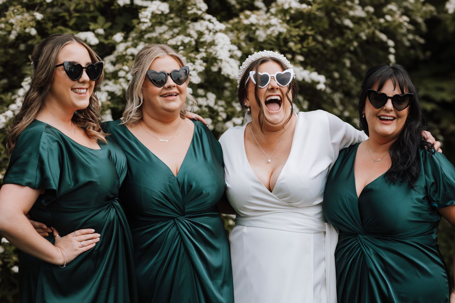 Wedding party laughing together with bridesmaids in emerald green dresses and sunglasses.