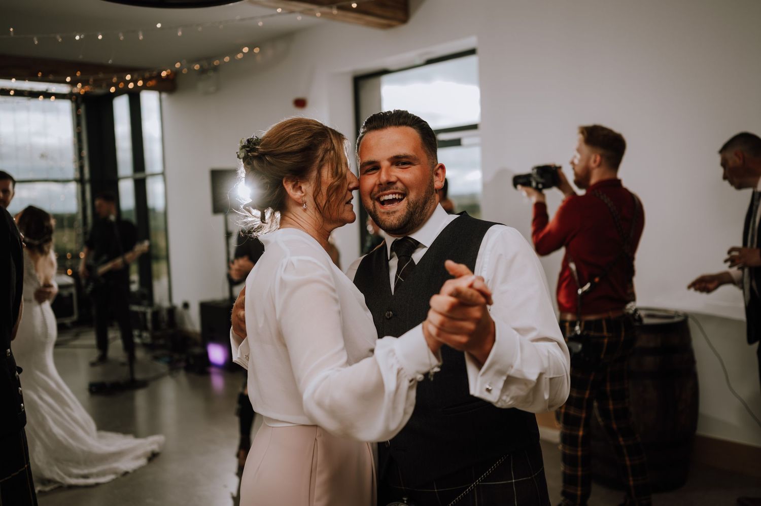 Joyful couple dancing together at their wedding reception in a modern venue with string lights.