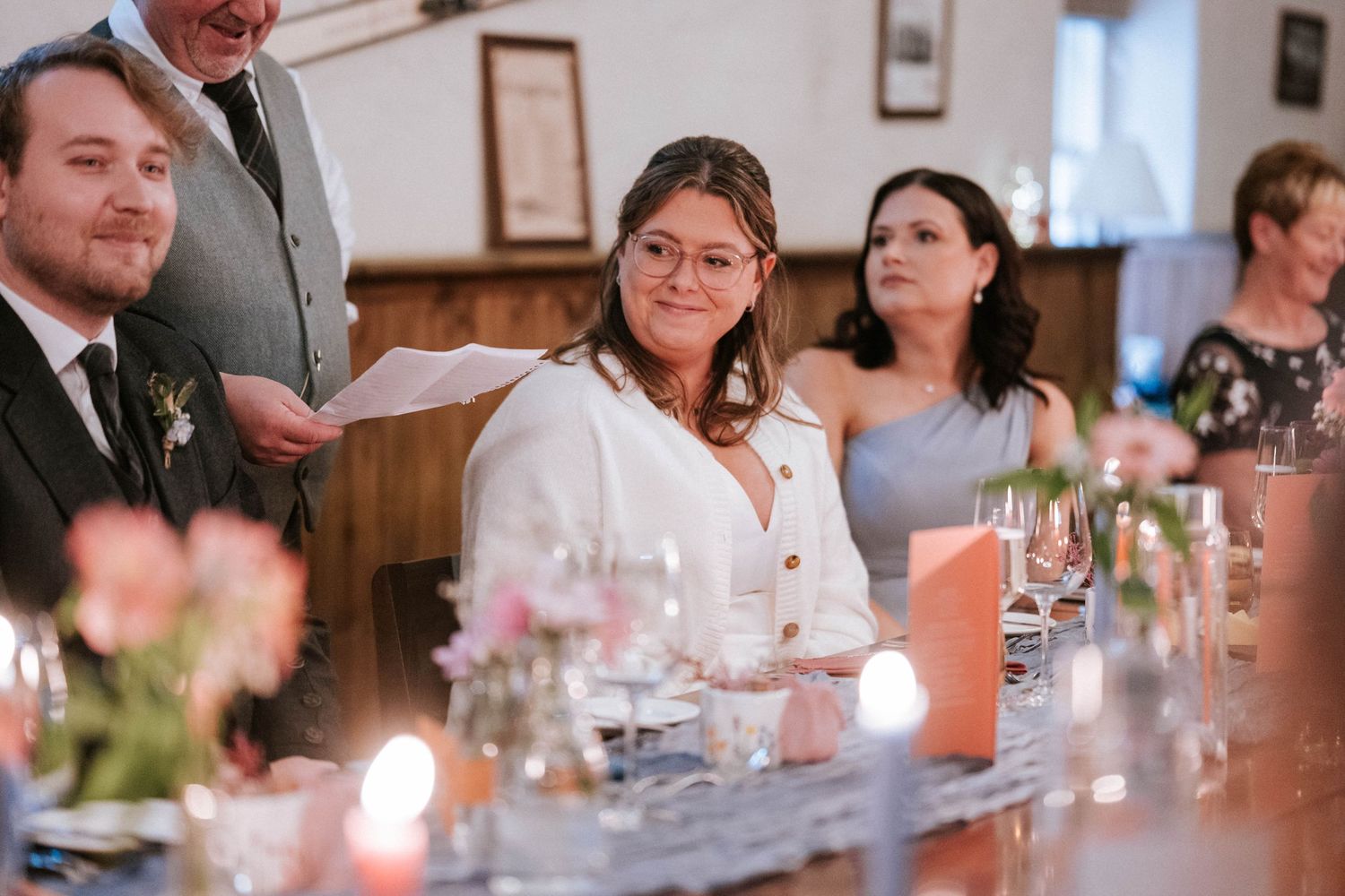 Wedding reception dinner table with guests and soft ambient lighting.